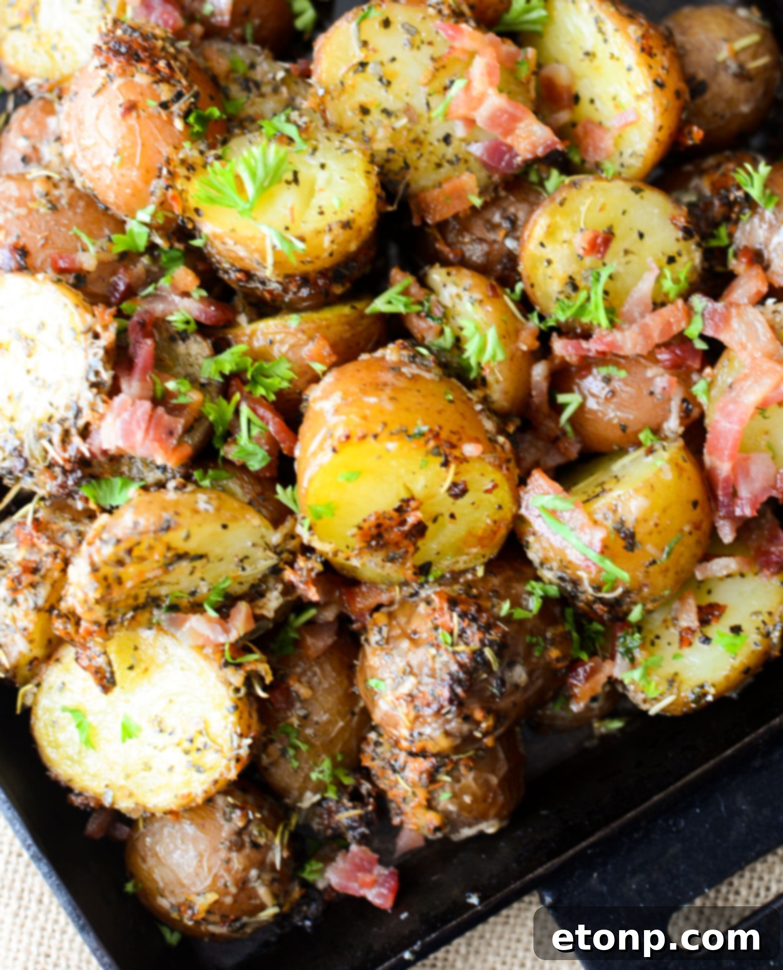 Hand sprinkling chopped fresh parsley over a batch of Parmesan Crusted Roasted Potatoes in a baking dish.