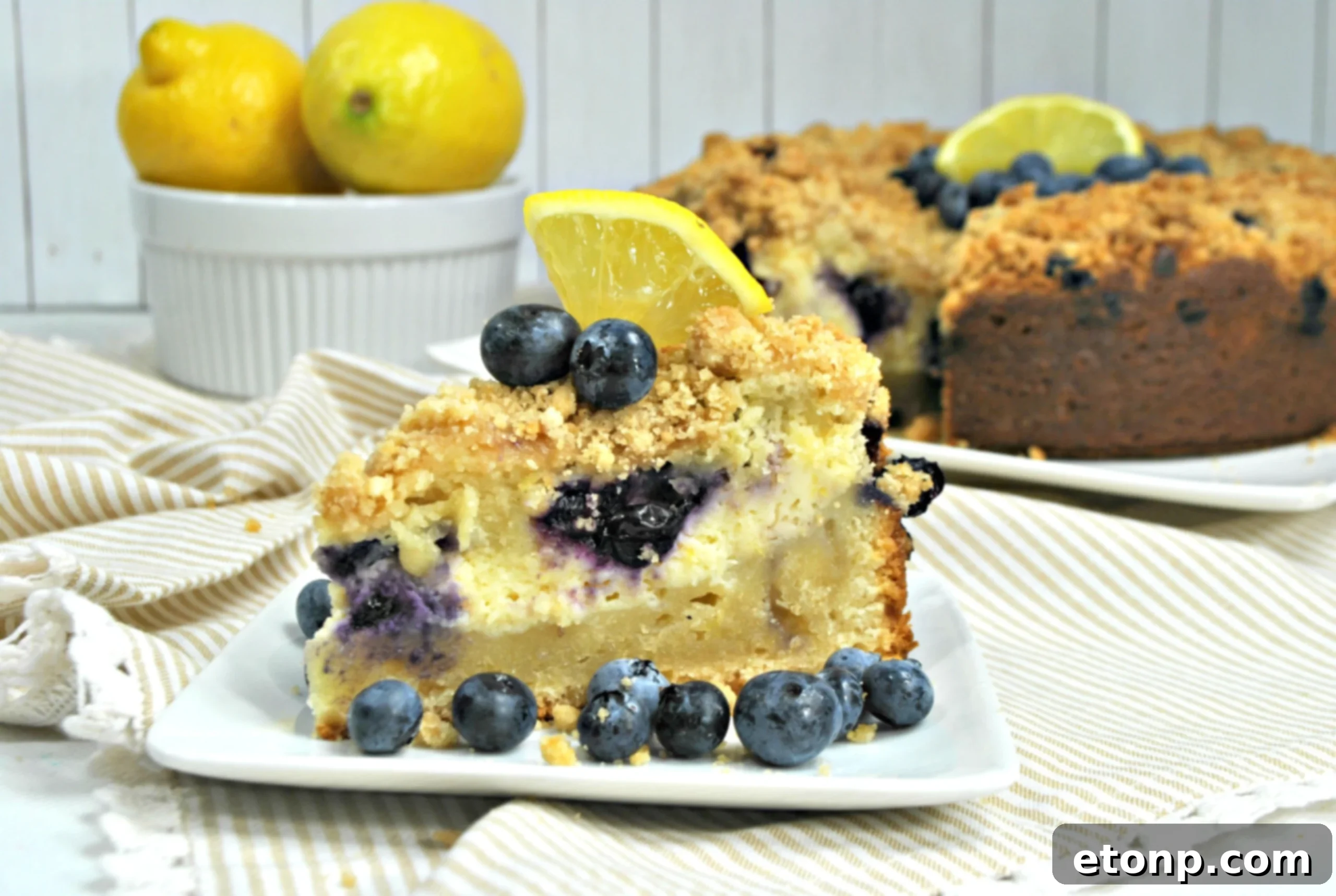 A large slice of Blueberry Cream Cheese Coffee Cake on a white plate, accompanied by a steaming cup of coffee.
