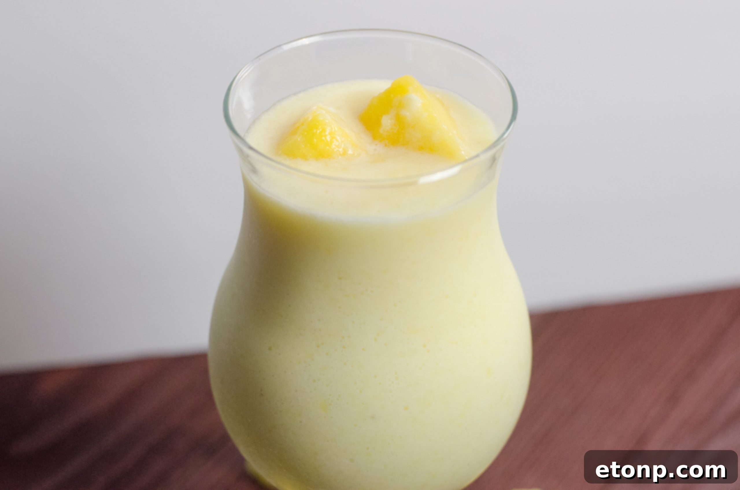 Close-up of a vibrant Drunken Disney Dole Pineapple Whip Margarita in a glass, with a lime wedge.