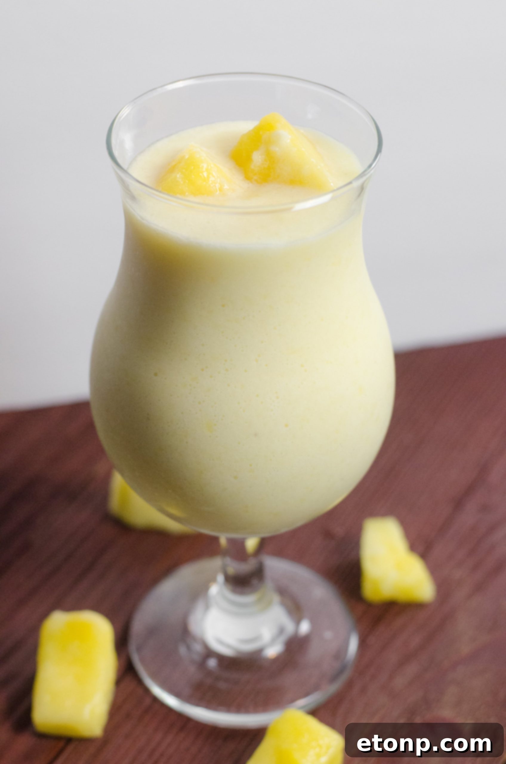 Two glasses of Drunken Disney Dole Pineapple Whip Margarita, one with a cherry, on a wooden surface.