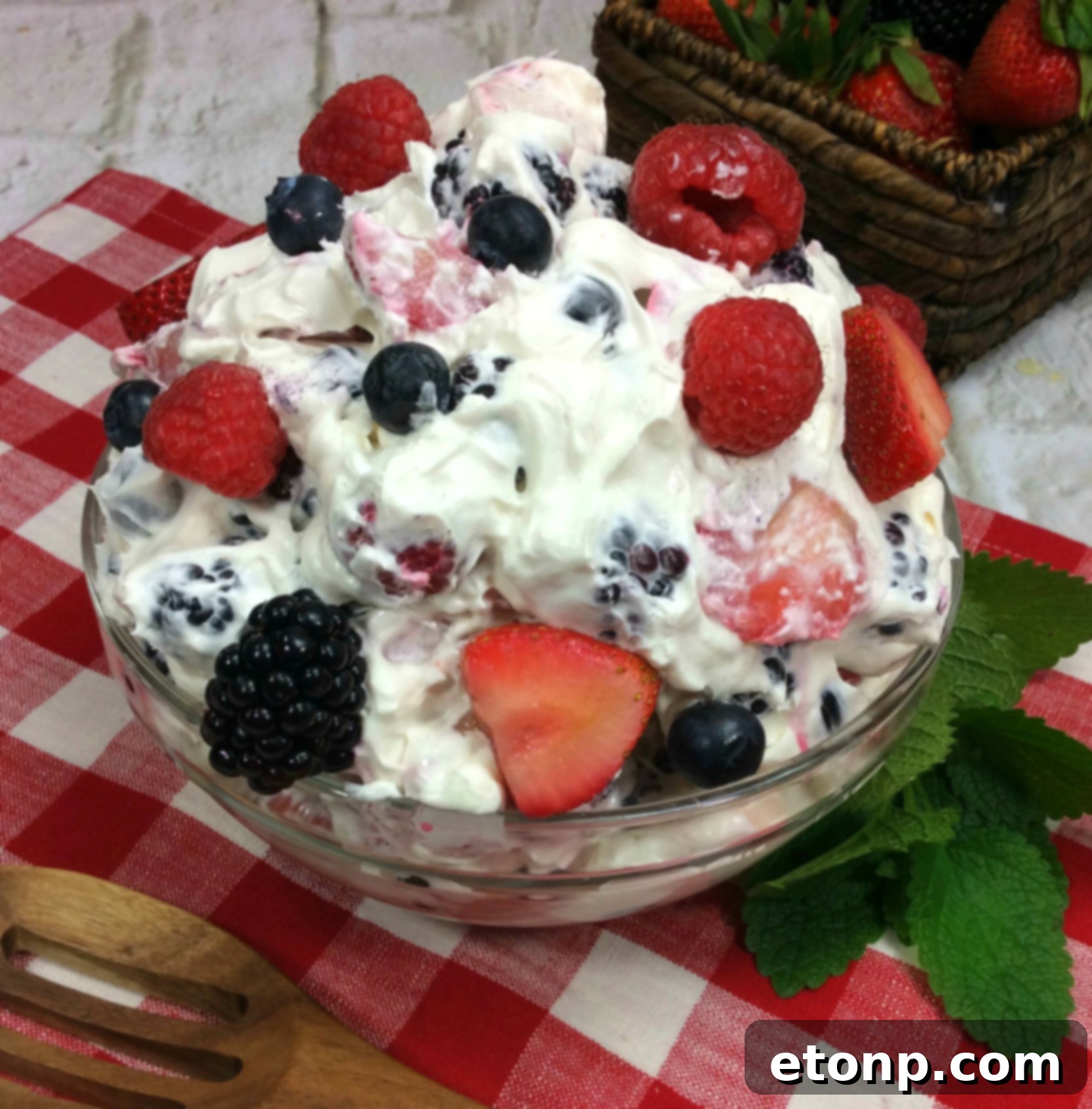 A large bowl of Cheesecake Summer Berry Salad overflowing with fresh strawberries, blueberries, raspberries, and blackberries, coated in a creamy white topping.