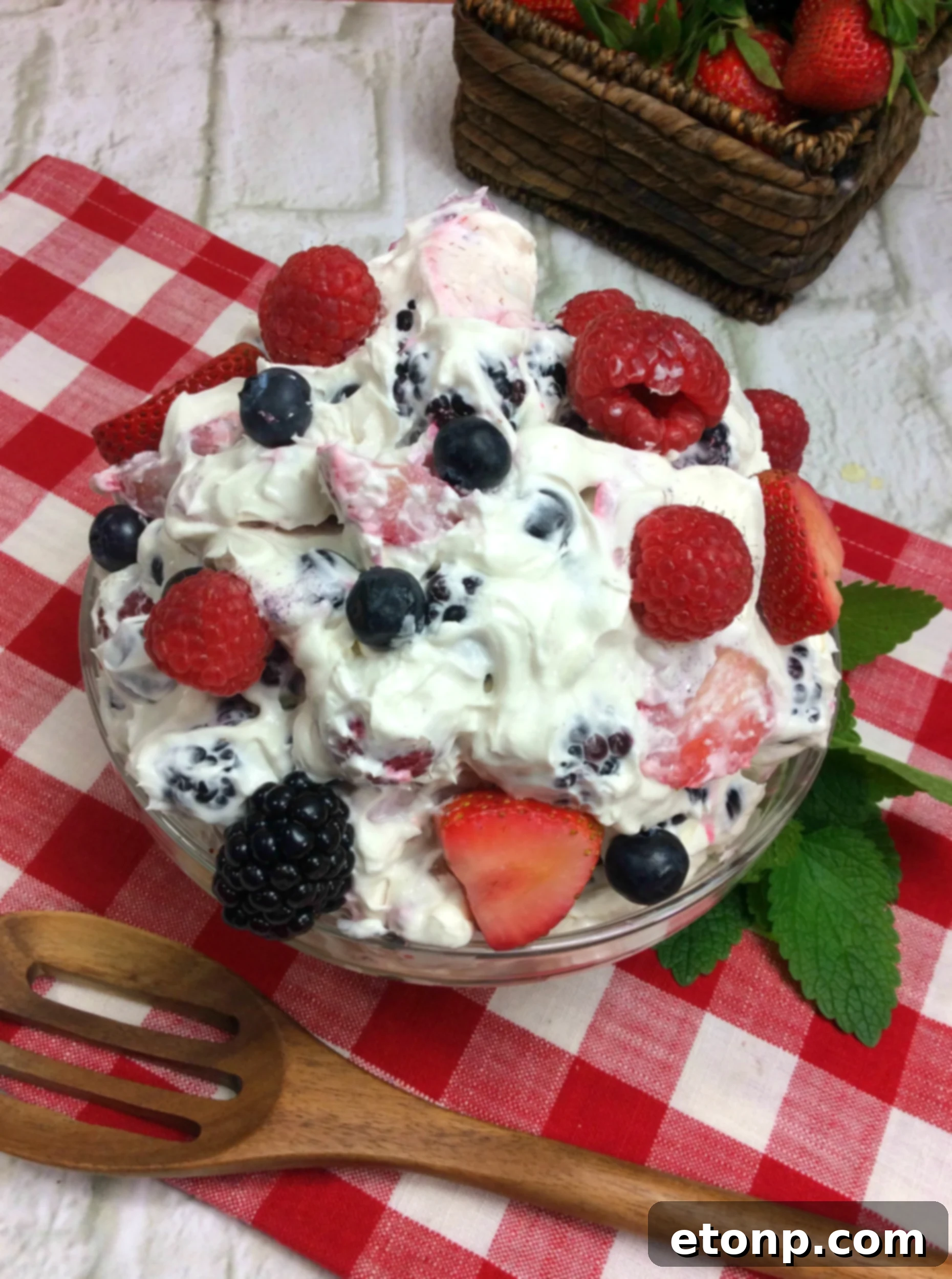 A close-up photo of a single serving of Cheesecake Summer Berry Salad in a small clear bowl, showcasing the layers of fruit and cream.