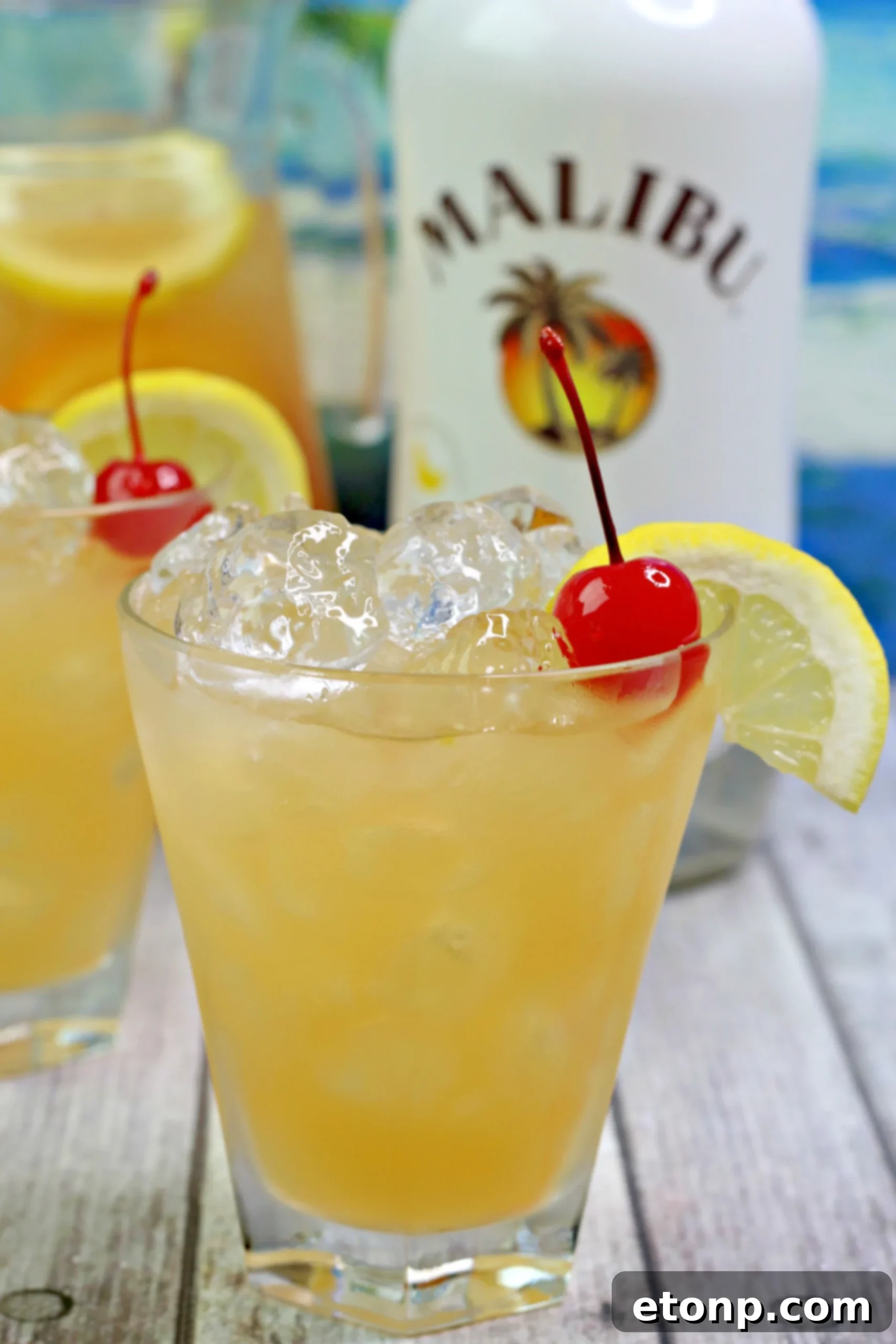A tall glass of vibrant yellow Banana Rum Punch, garnished with a fresh orange slice, a red cherry, and a green leaf, set on a dark background with blurred lights.