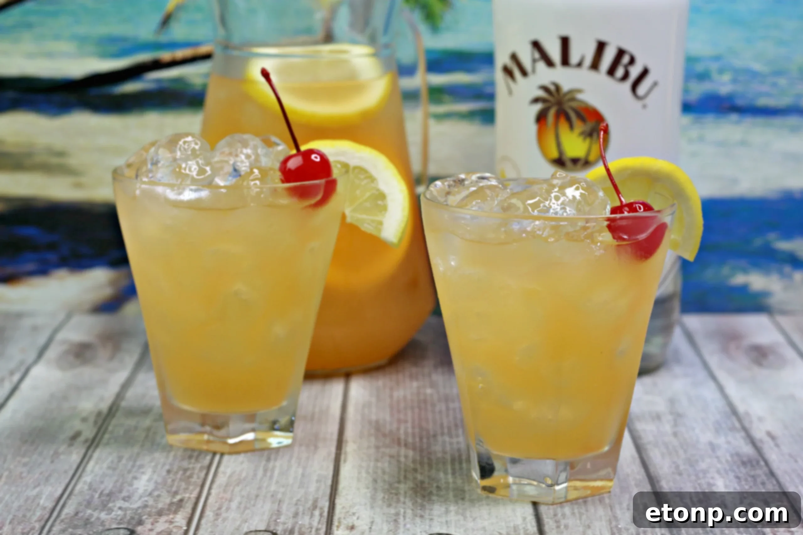 A close-up shot of a hand holding a glass of Banana Rum Punch, showing the fruit garnish and a straw, against a blurred background.
