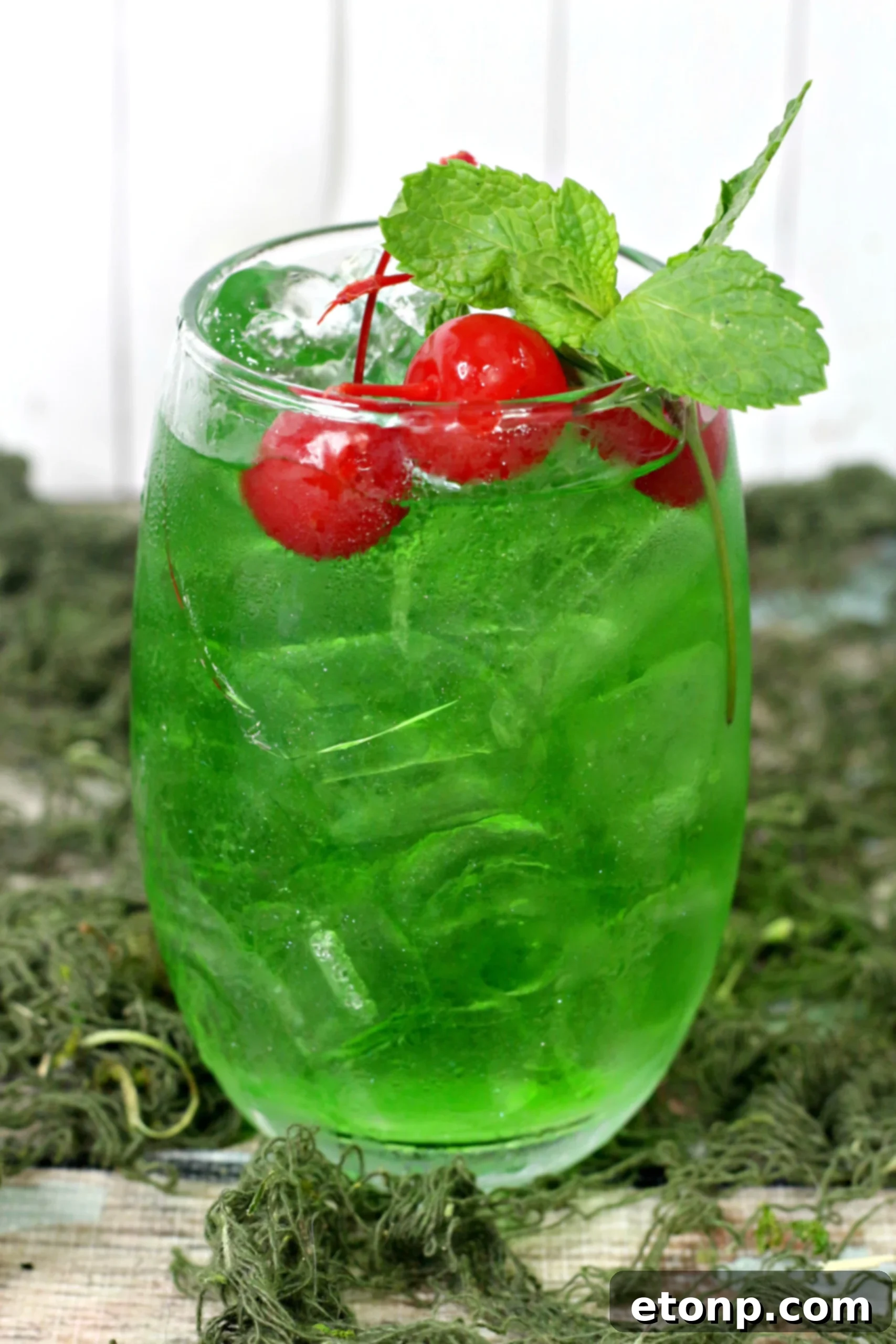 A Liquid Marijuana Cocktail in a tall glass, adorned with a lime wedge and apple slices, set against a vibrant background
