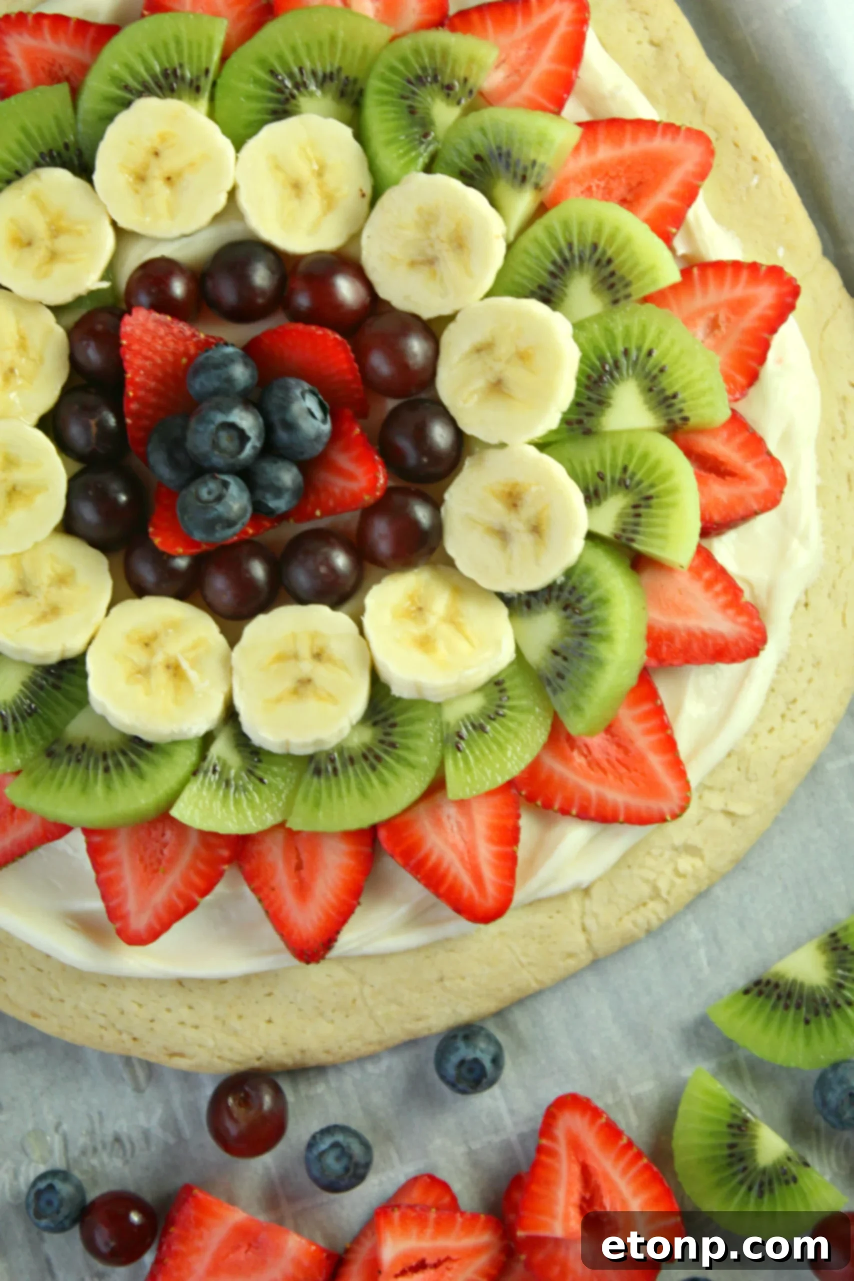 A beautifully arranged fruit pizza, showcasing a vibrant assortment of fresh berries, kiwi, and oranges on a sweet sugar cookie crust with cream cheese frosting.