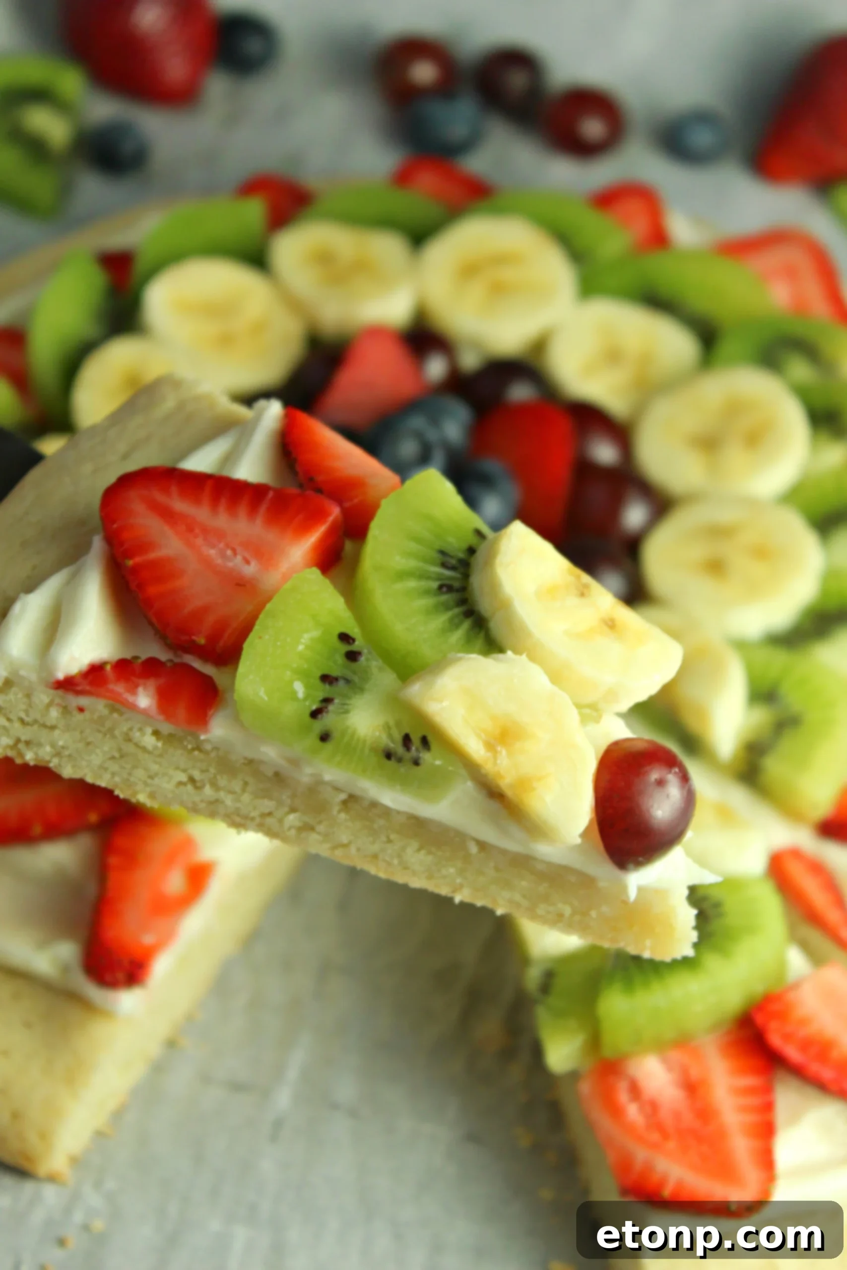 A vibrant fruit pizza decorated with blueberries, strawberries, kiwi, and grapes, arranged in an appealing pattern.