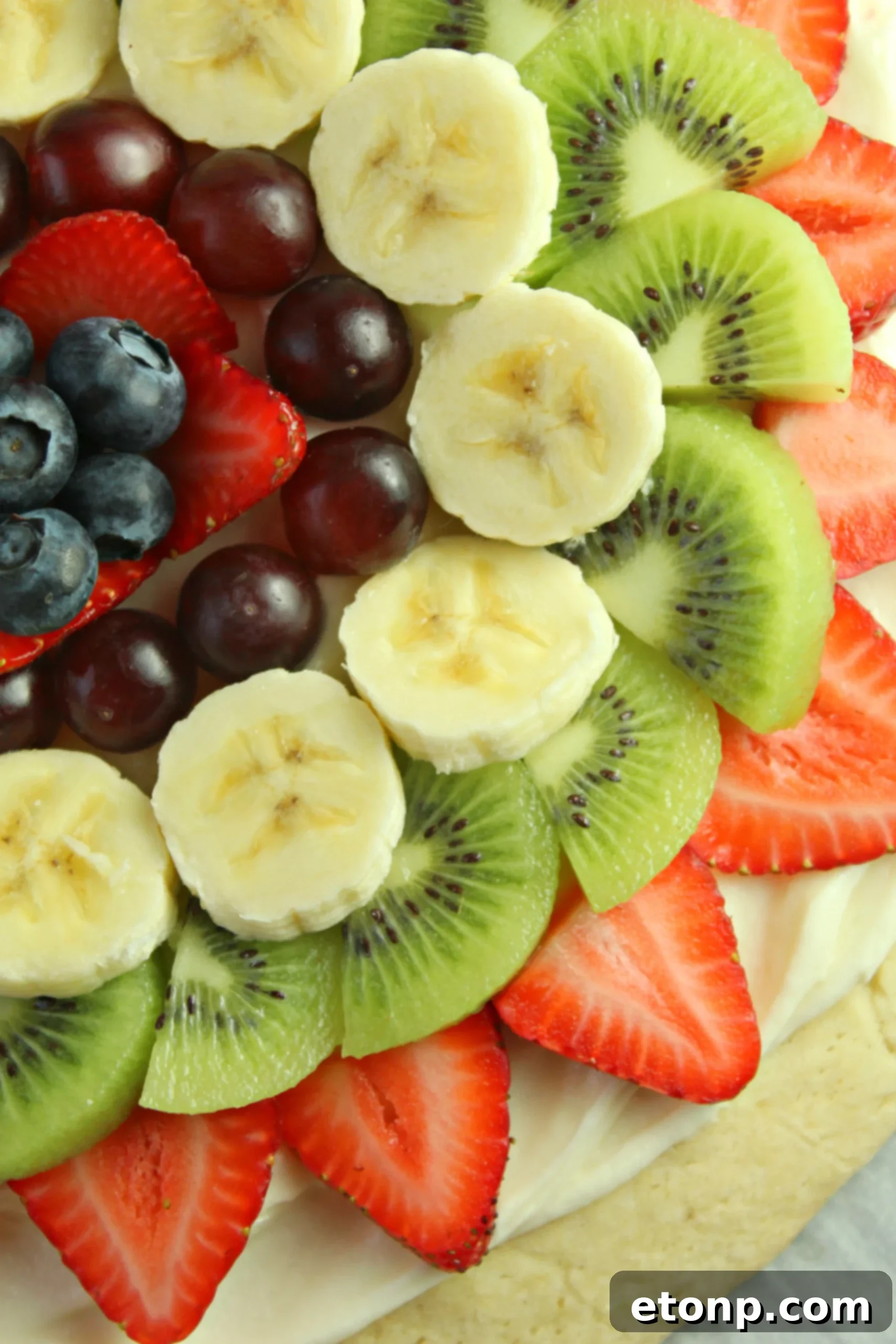 A selection of fresh, colorful fruits laid out on paper towels, prepared for topping a fruit pizza.