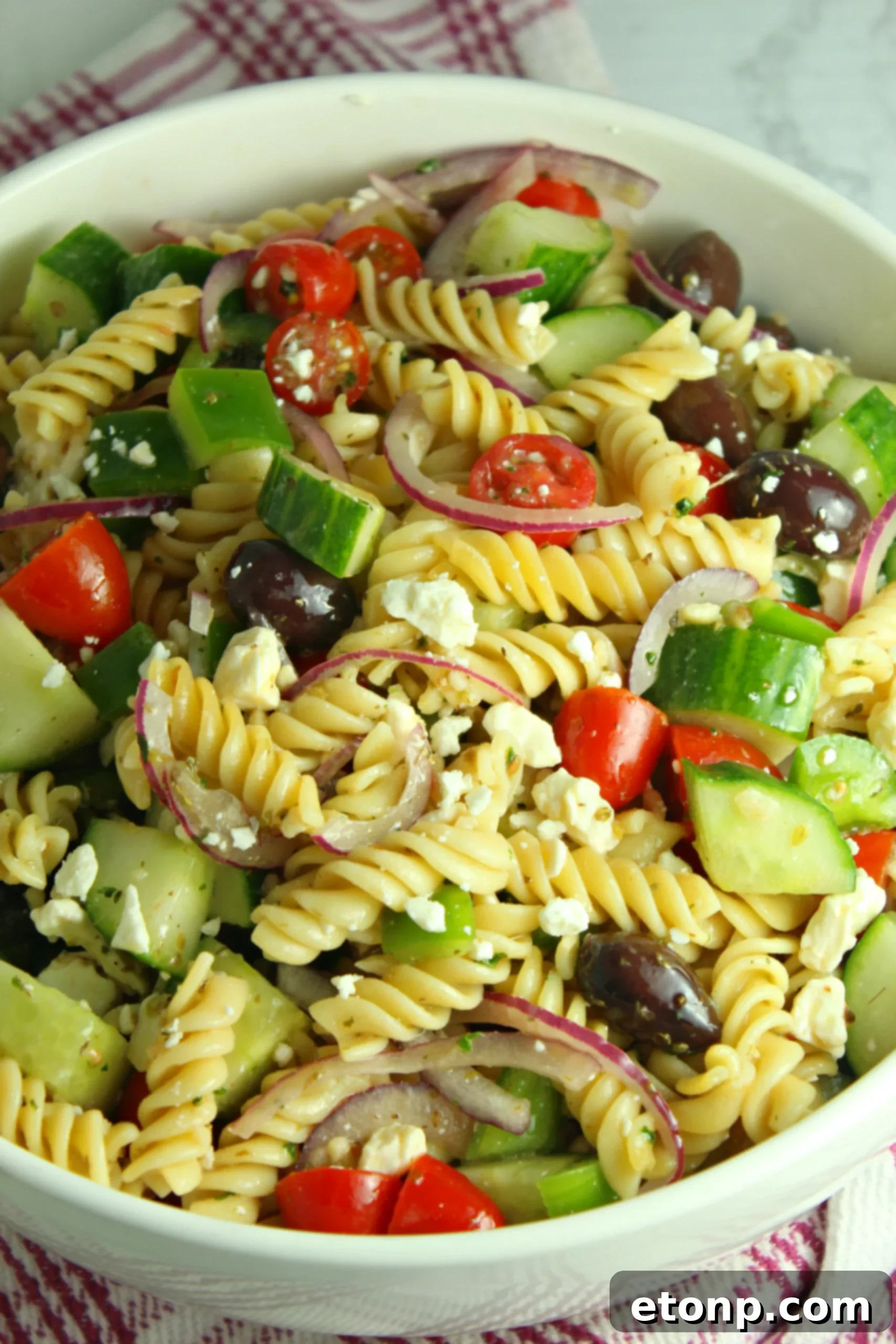 A vibrant bowl of Greek Pasta Salad featuring rotini pasta, fresh vegetables like cucumber, cherry tomatoes, and red onion, and crumbled feta cheese, with a light dressing.