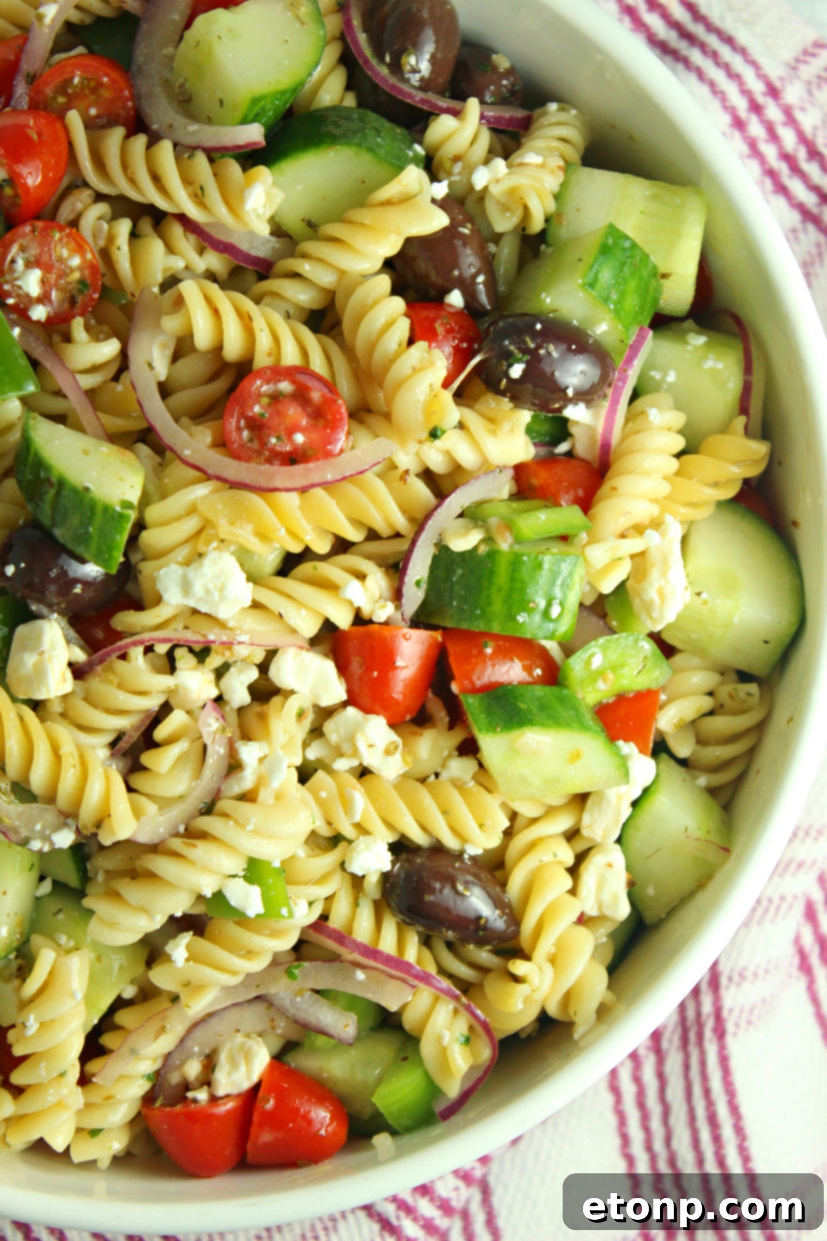 Greek Pasta Salad being tossed with dressing in a large bowl.