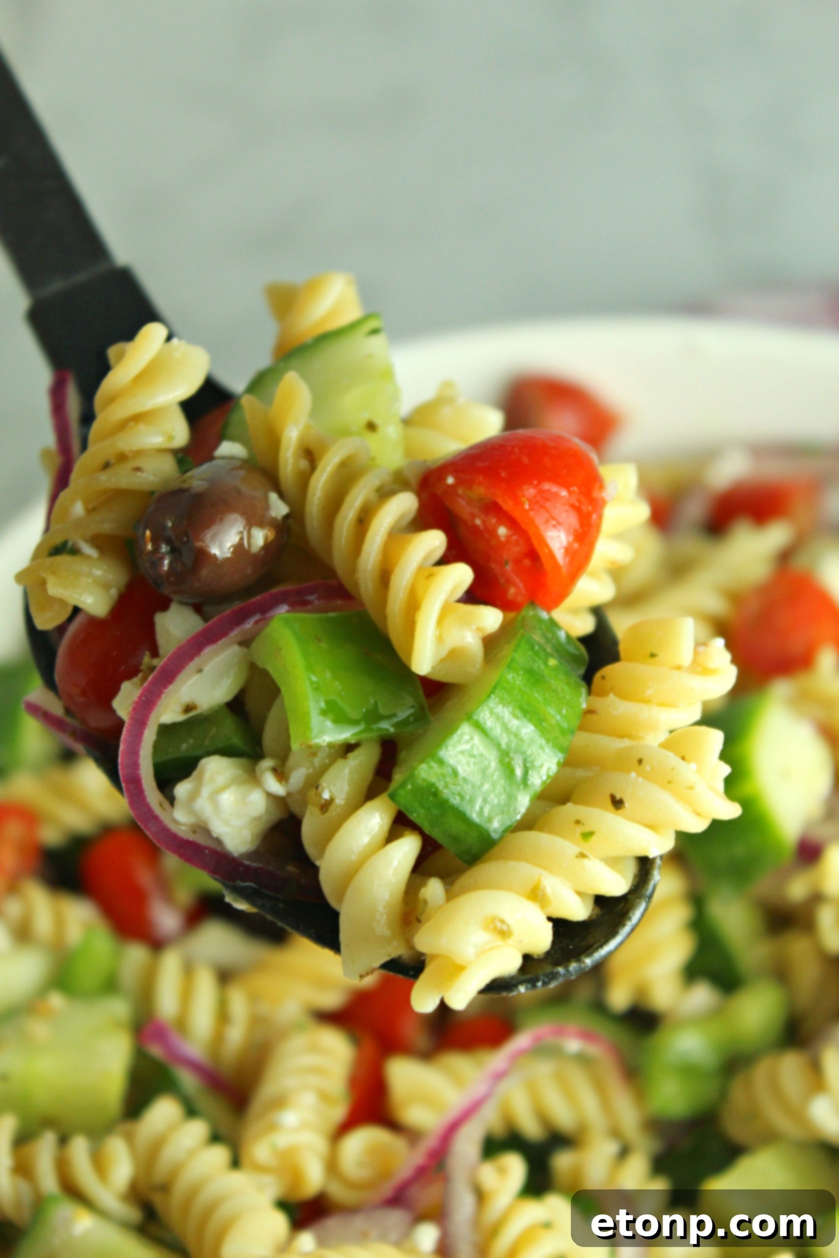 A serving of Greek Pasta Salad in a smaller white bowl, garnished with a sprig of fresh parsley.
