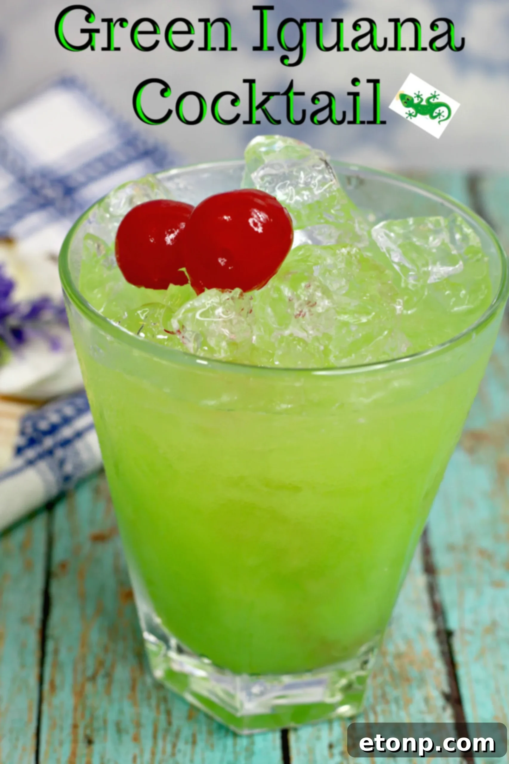 Emerald Iguana Elixir 2 Green Iguana Cocktail in a hurricane glass, garnished with a lime wedge and cherry, against a blurred tropical background.