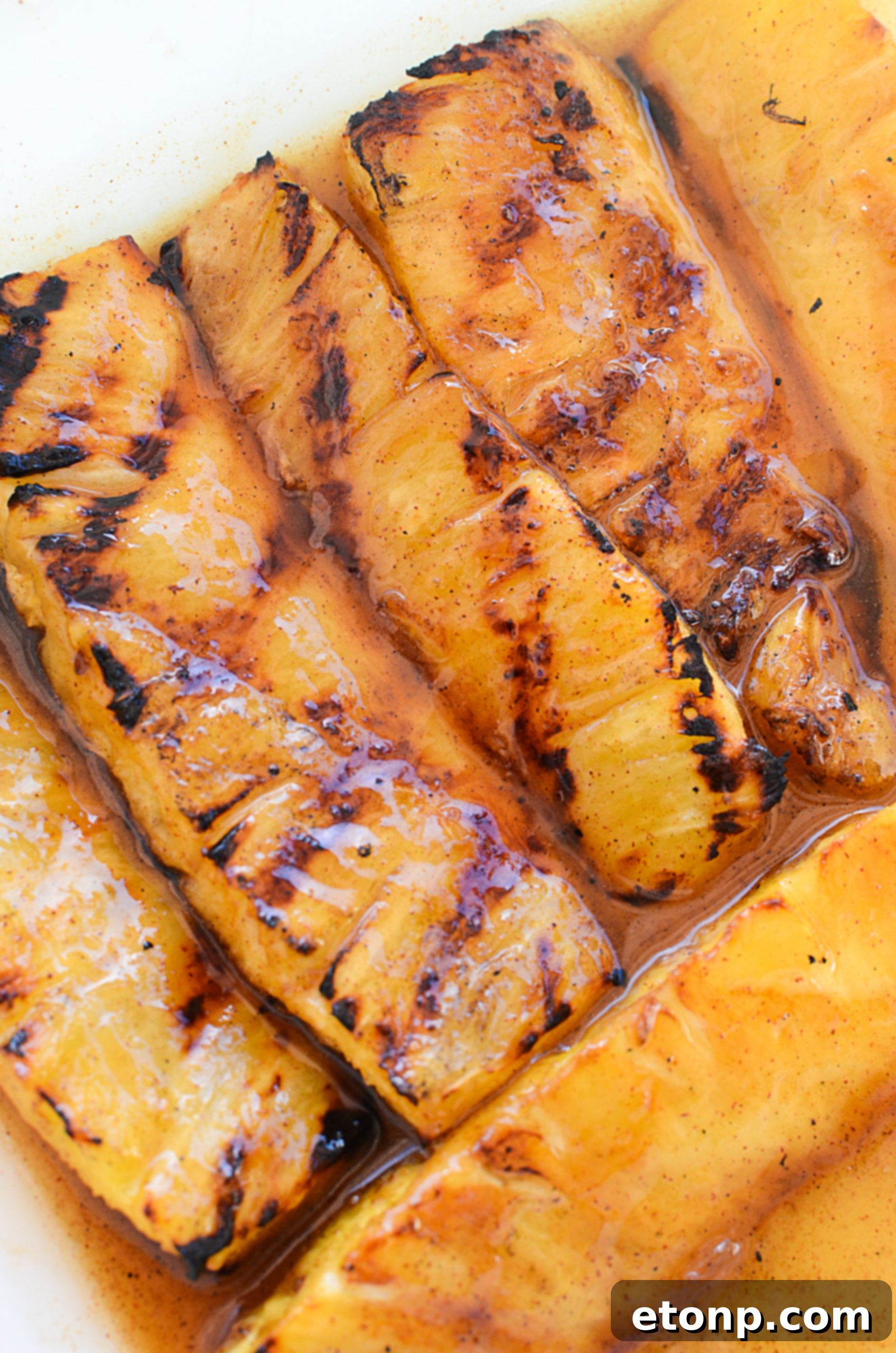 A hand basting grilled pineapple spears on the grill with a brush