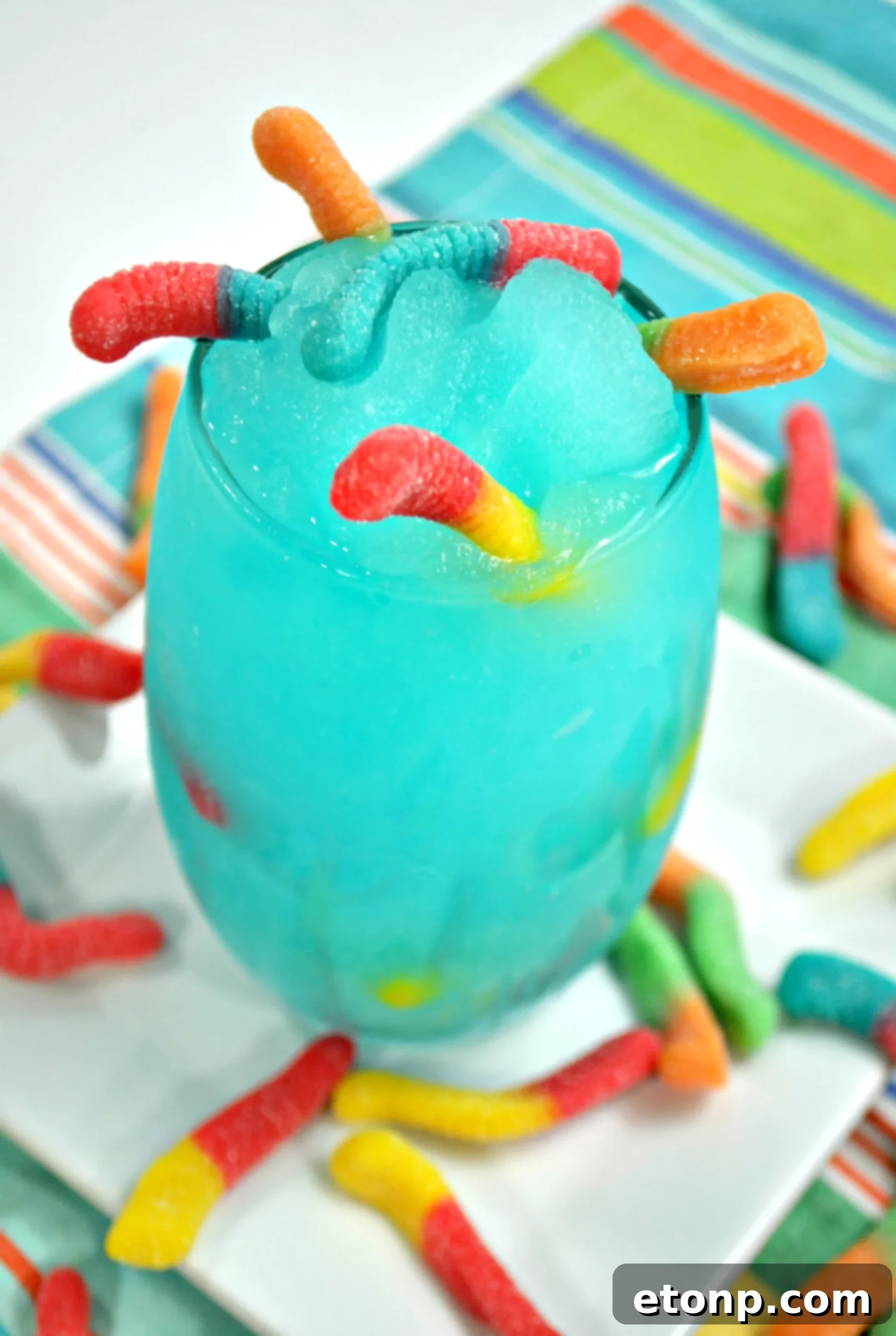 Vibrant Drunken Sour Gummy Worm Cocktail in a tall glass with gummy worm garnish