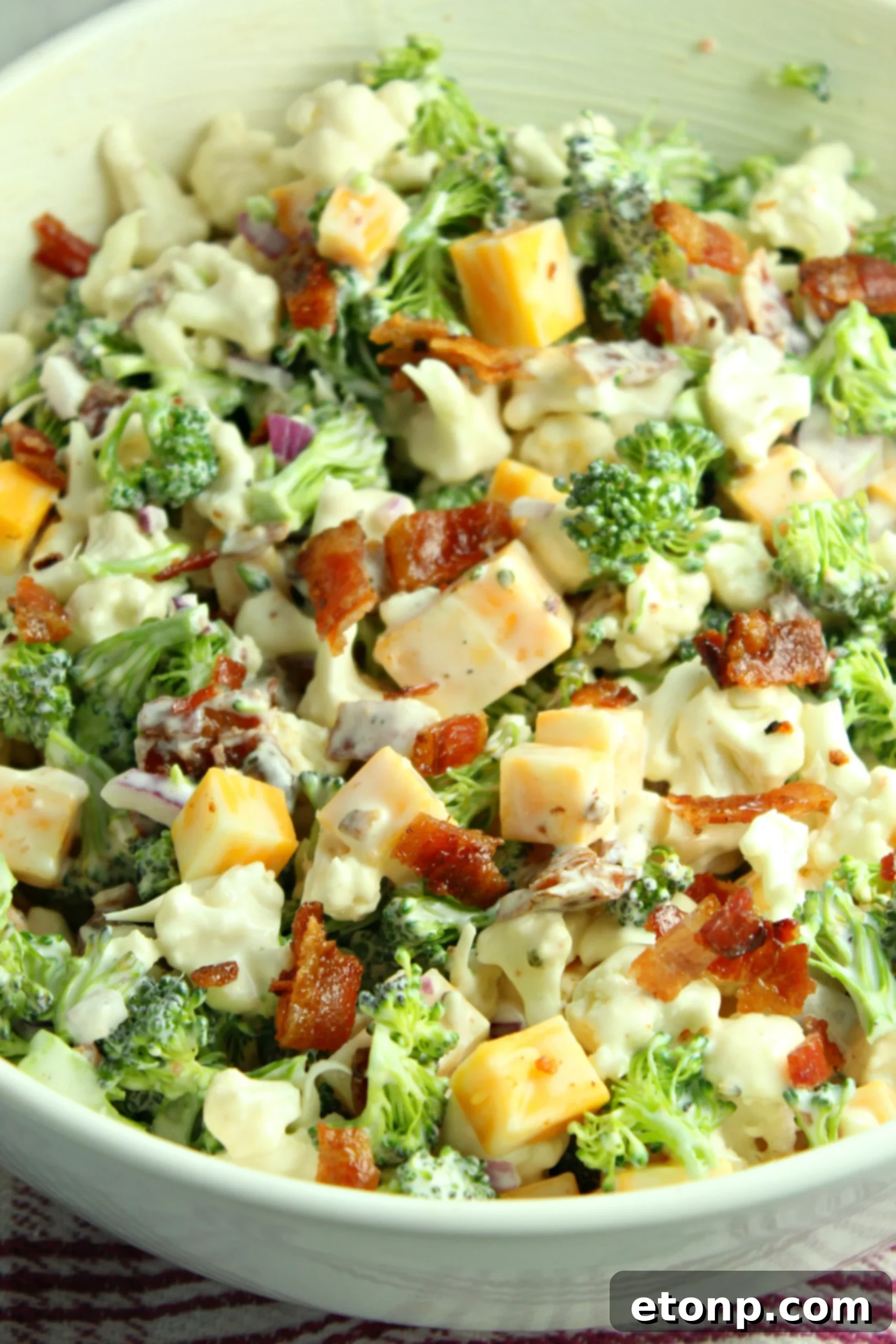 Rich and Flavorful Low Carb Broccoli Cauliflower Salad 2 Close-up of a vibrant Loaded Broccoli Cauliflower Salad with crispy bacon bits, cheddar cheese cubes, and creamy dressing in a white bowl.