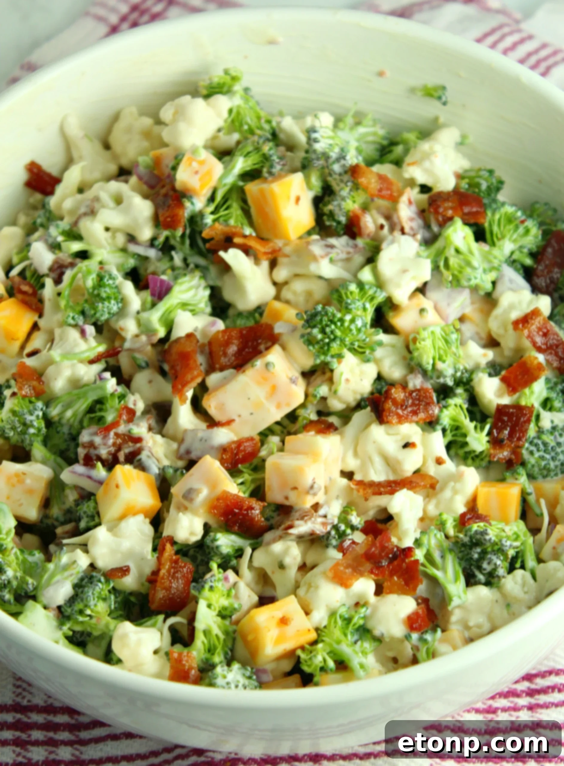 Rich and Flavorful Low Carb Broccoli Cauliflower Salad 4 A bowl of Loaded Broccoli Cauliflower Salad placed on an outdoor table, ready to be served at a BBQ, with other dishes blurred in the background.