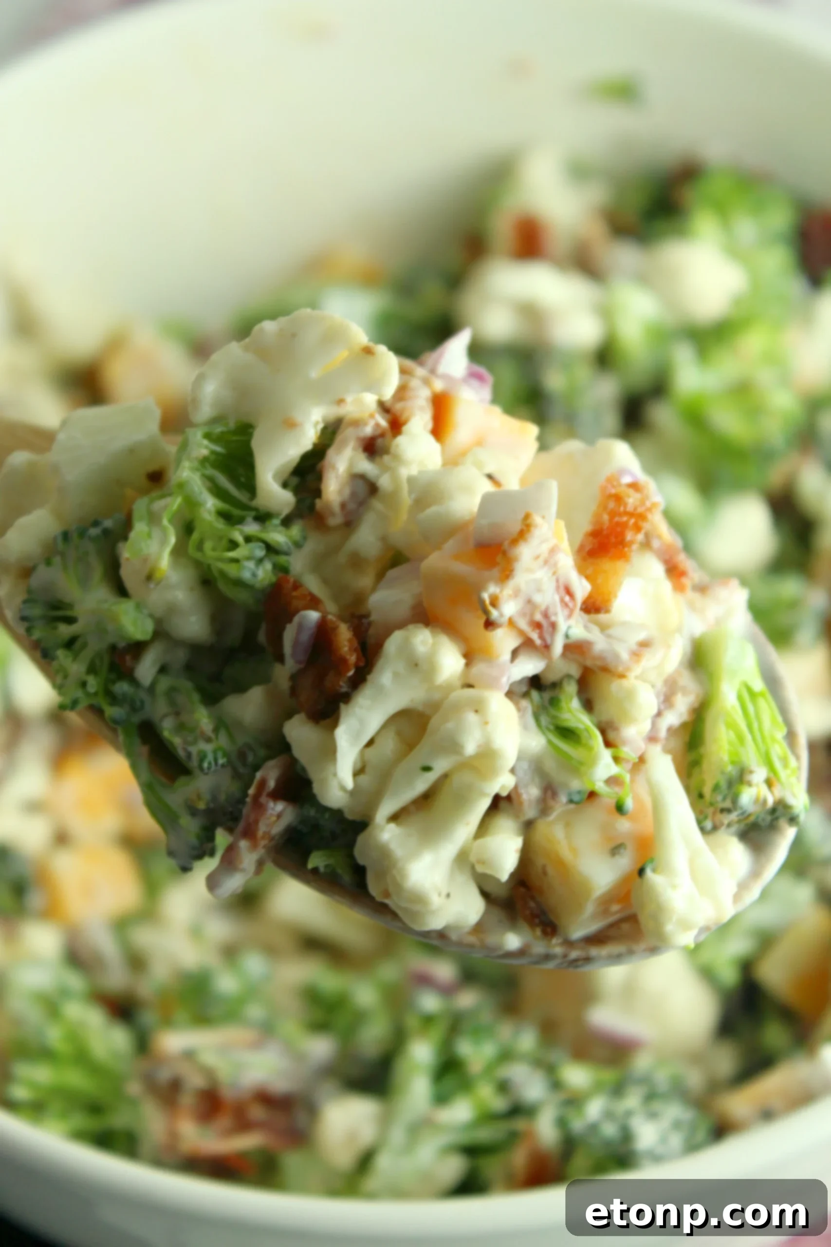 Rich and Flavorful Low Carb Broccoli Cauliflower Salad 7 A large glass bowl of freshly prepared Loaded Broccoli Cauliflower Salad, with a serving spoon, ready to be covered and chilled.