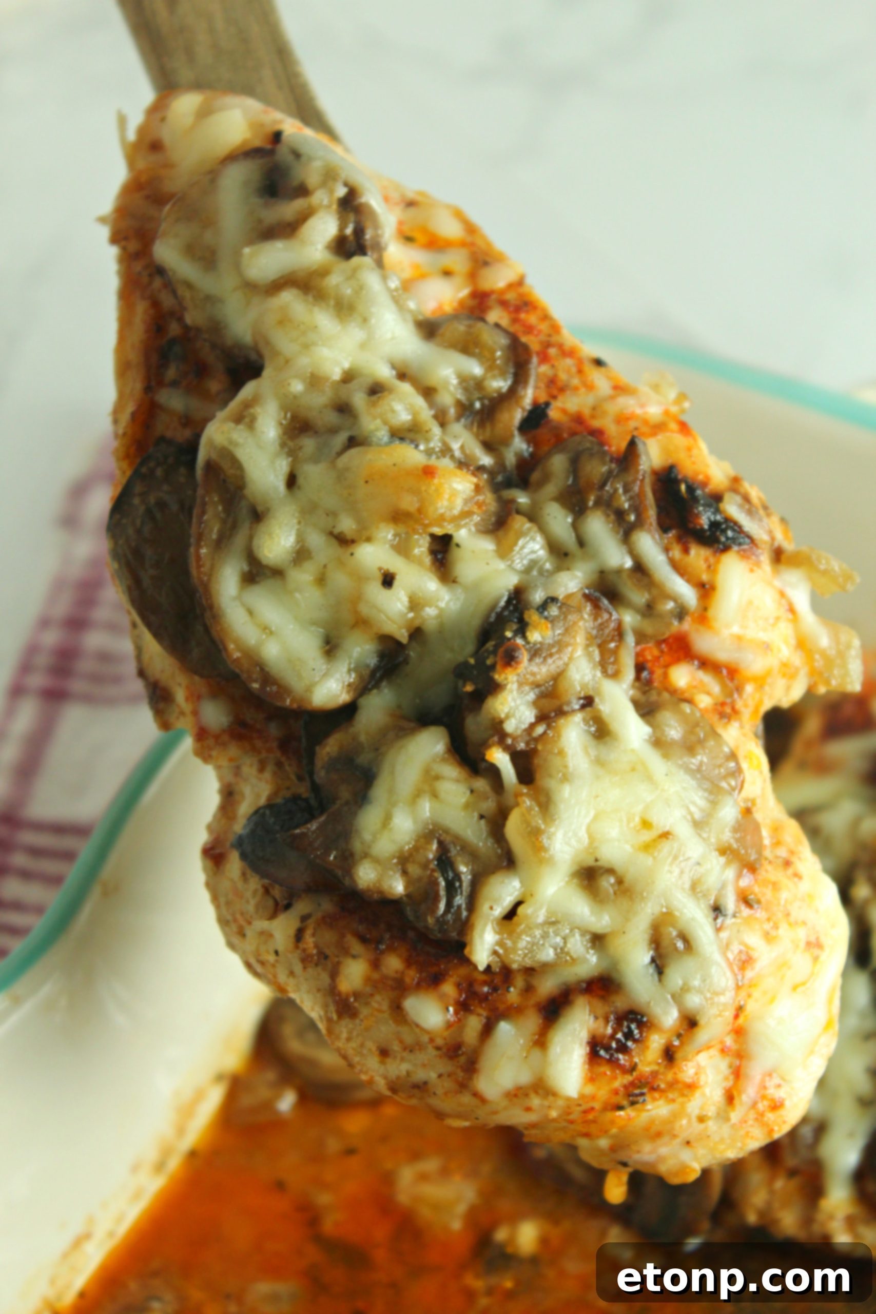 Close-up of baked chicken breast covered in sautéed mushrooms, caramelized onions, and melted cheese, showcasing the rich texture and golden crust.