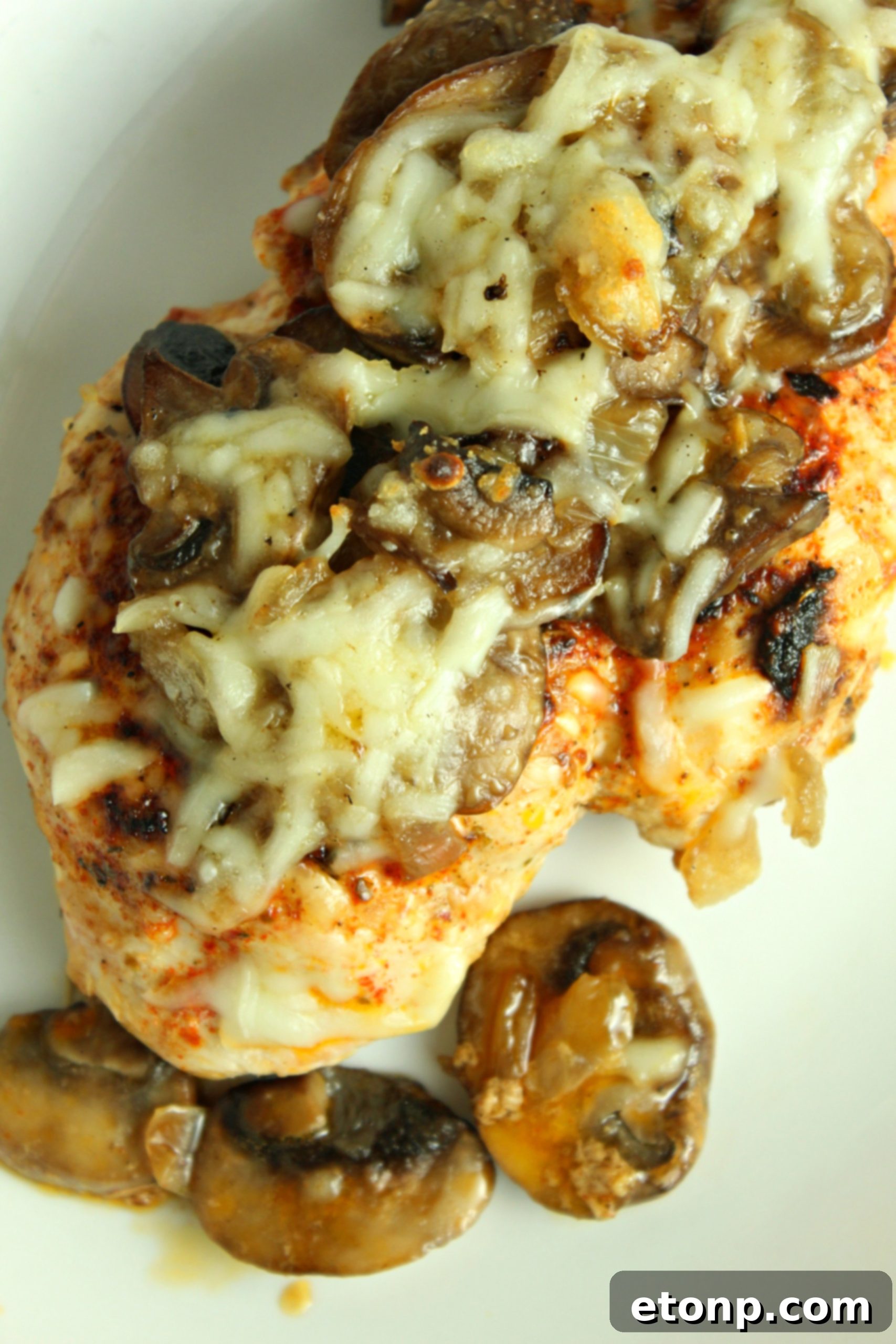 Smothered Cheesy Baked Chicken, showcasing the melted cheese and a glimpse of the tender chicken and mushroom mixture beneath.
