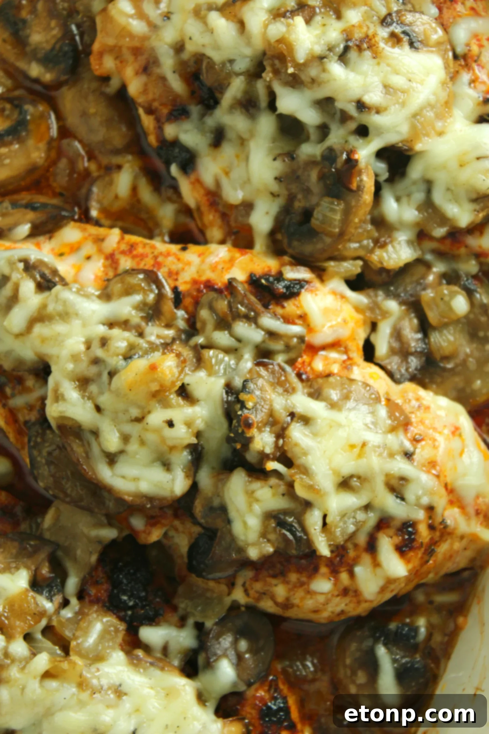 A perfectly cooked piece of Smothered Cheesy Baked Chicken, showing the layers of cheese, mushrooms, and tender chicken.