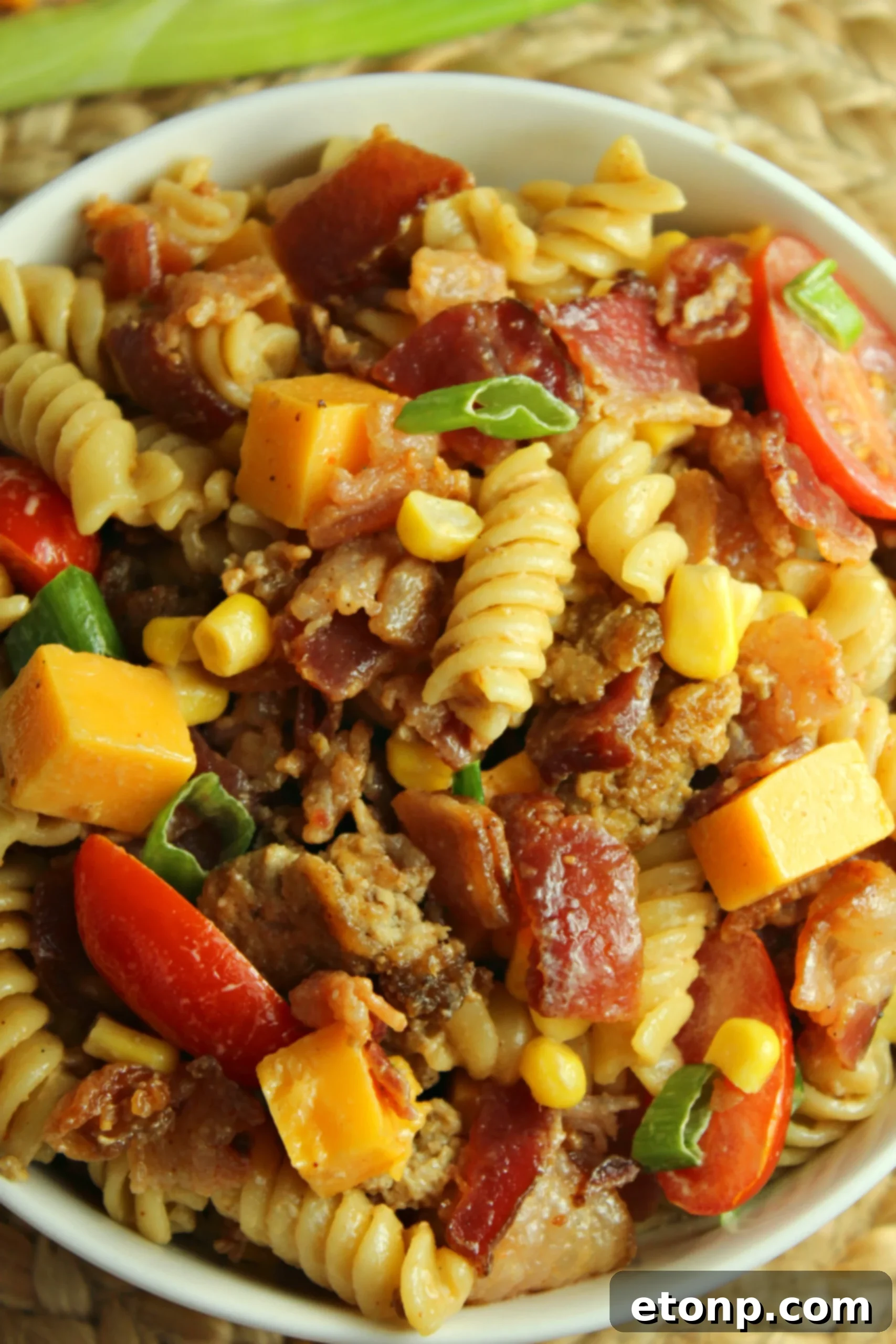 Chuckwagon Pasta Salad 2 A vibrant bowl of Loaded Cowboy Pasta Salad with rotini, bacon, ground beef, corn, tomatoes, and cheese, garnished with green onions.