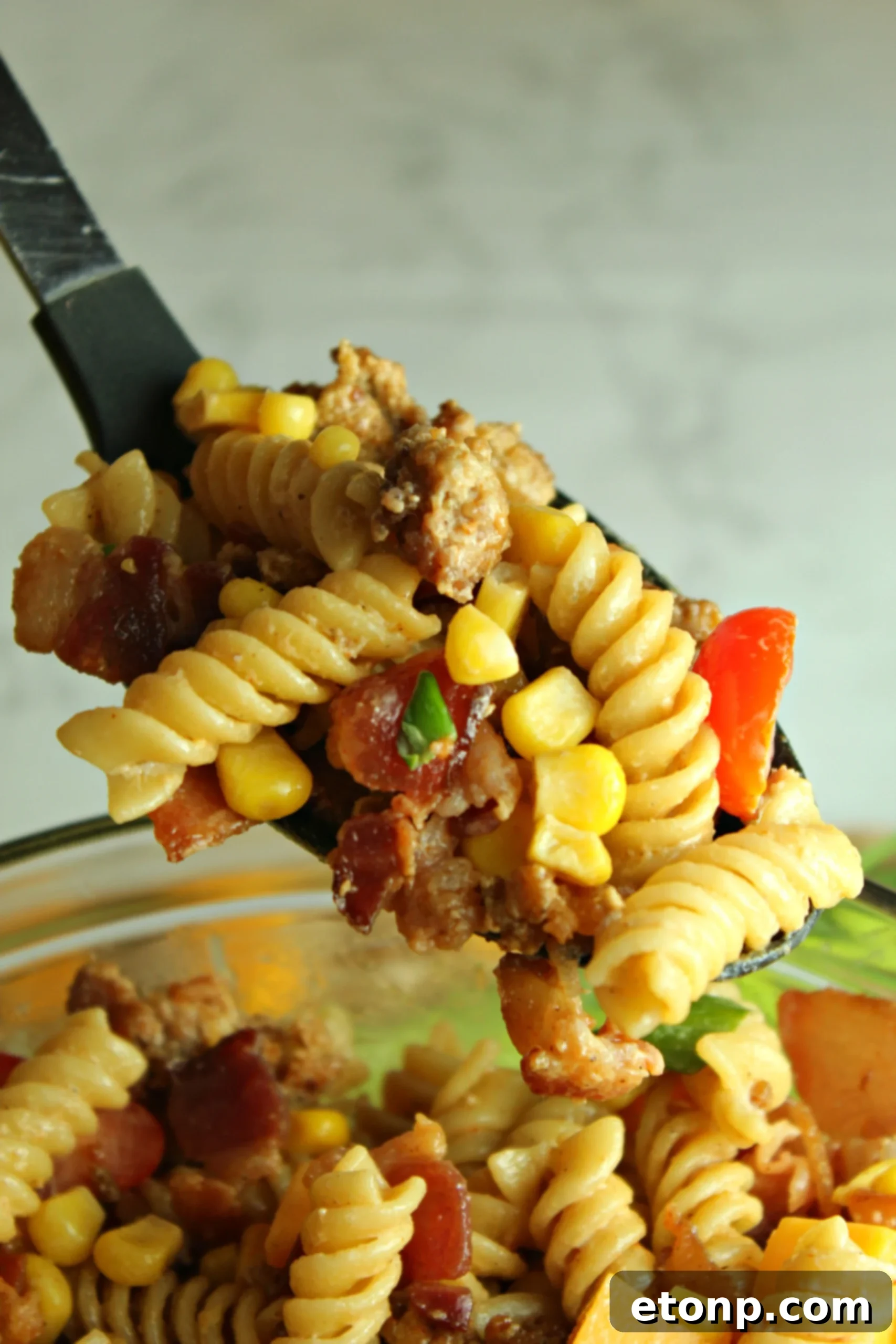 Chuckwagon Pasta Salad 6 A large serving spoon scooping a generous portion of the Loaded Cowboy Pasta Salad from a bowl, emphasizing its heartiness.