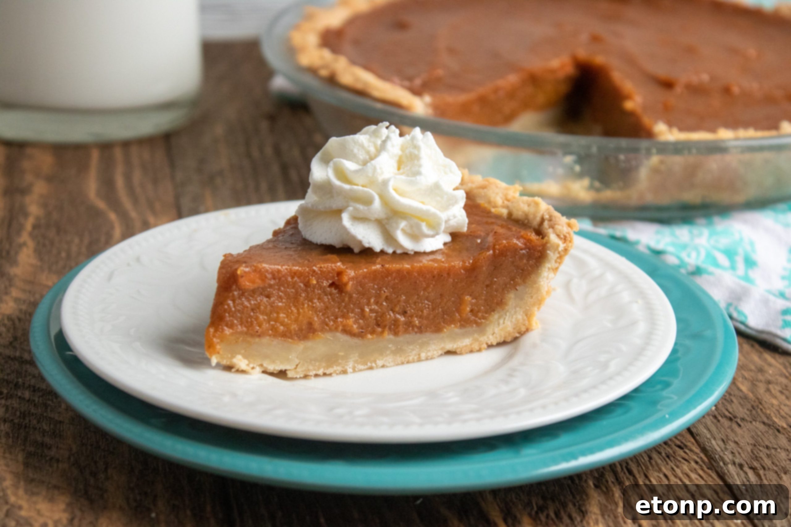 A slice of sweet potato pie with a dollop of whipped cream and a sprinkle of cinnamon.