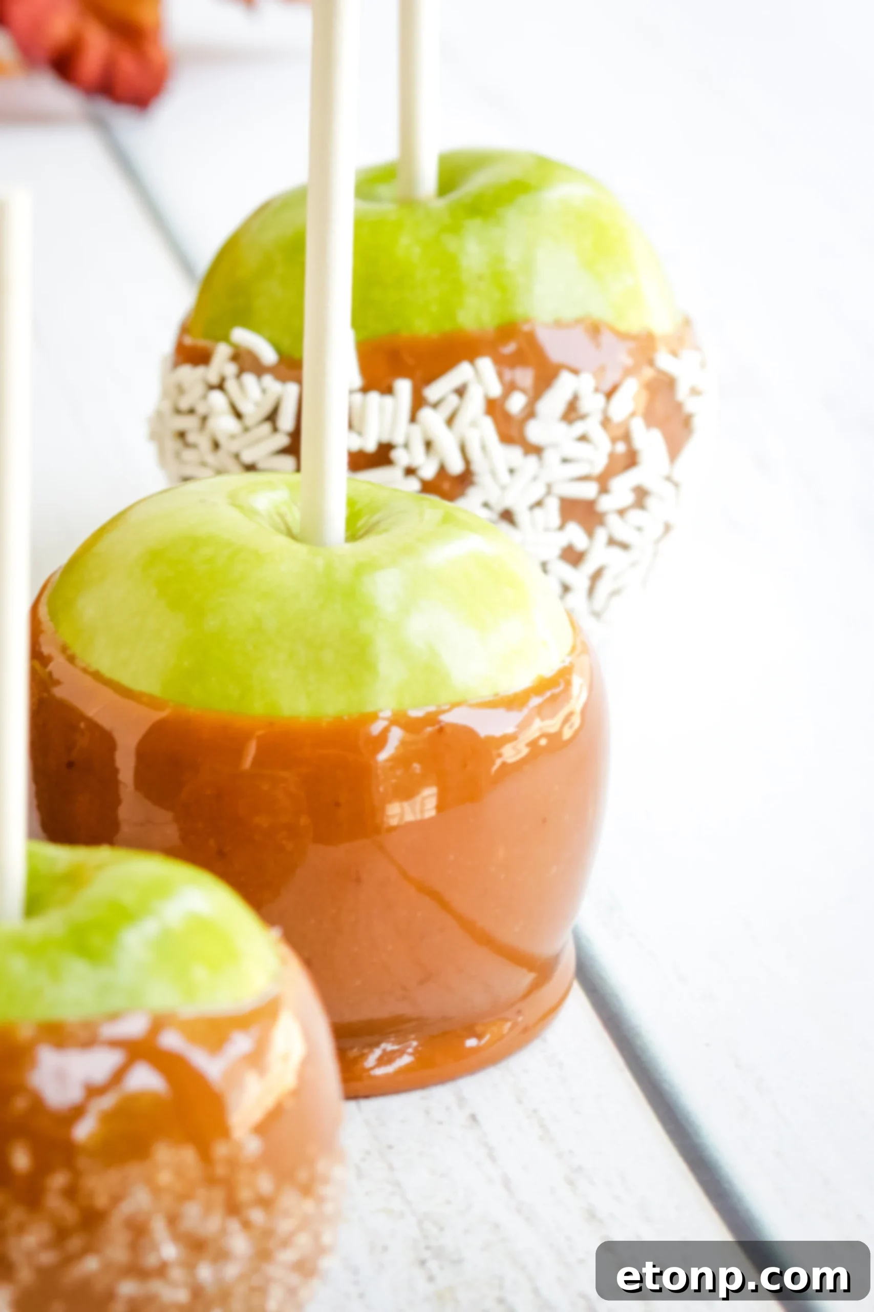 A batch of homemade caramel apples, some already coated and others waiting for toppings