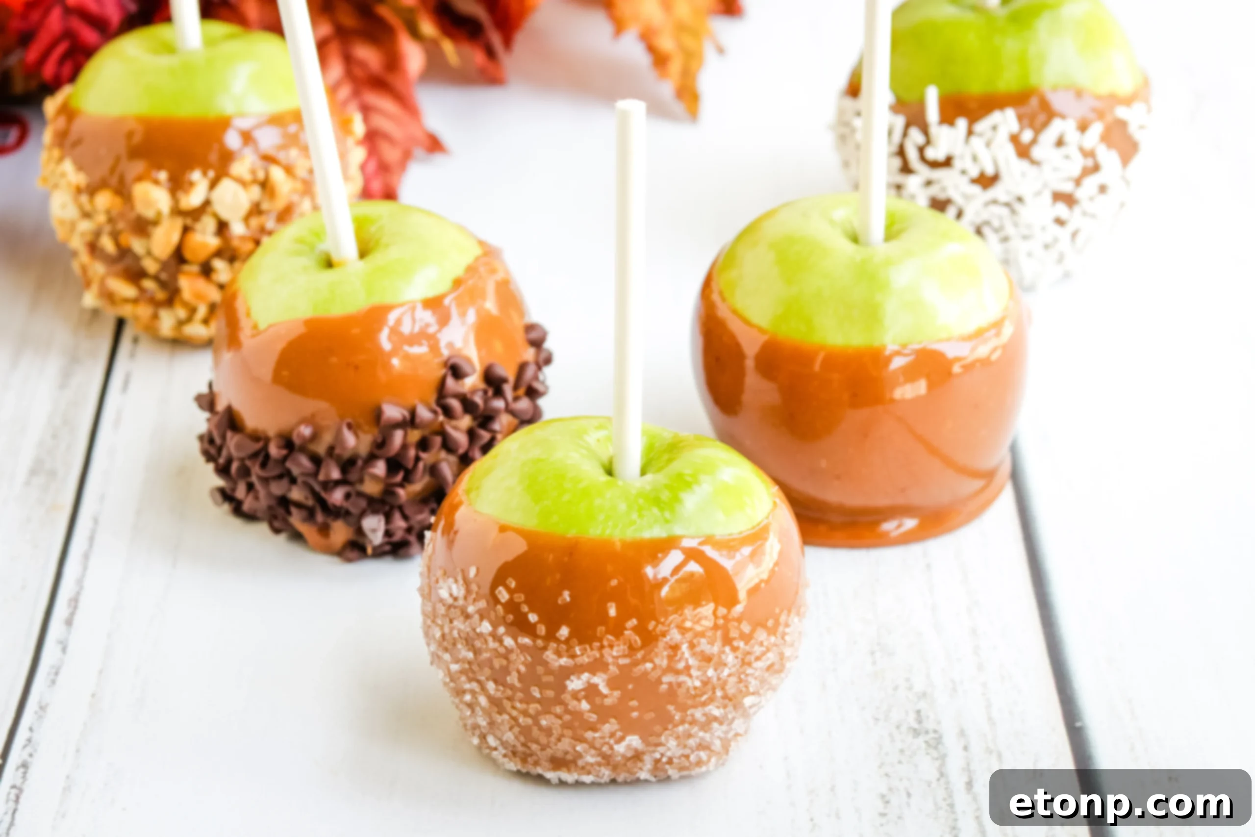 Two hands decorating a caramel apple with colorful sprinkles, showcasing customization options