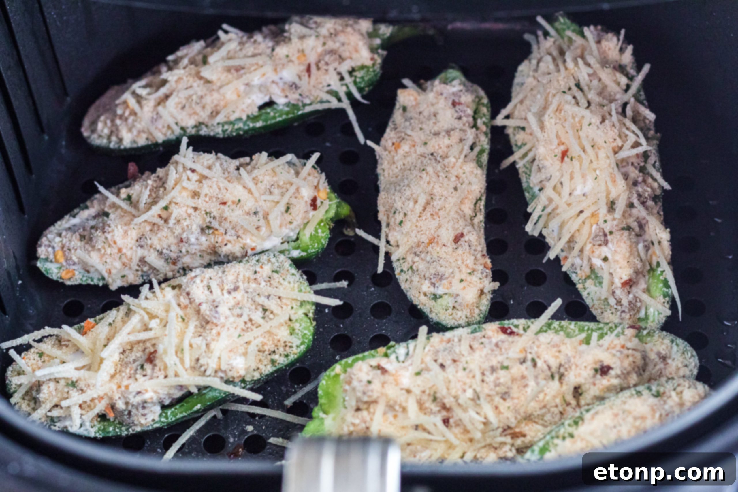 Close-up view of halved jalapenos filled with a creamy cheese and sausage mixture, ready for coating and air frying.