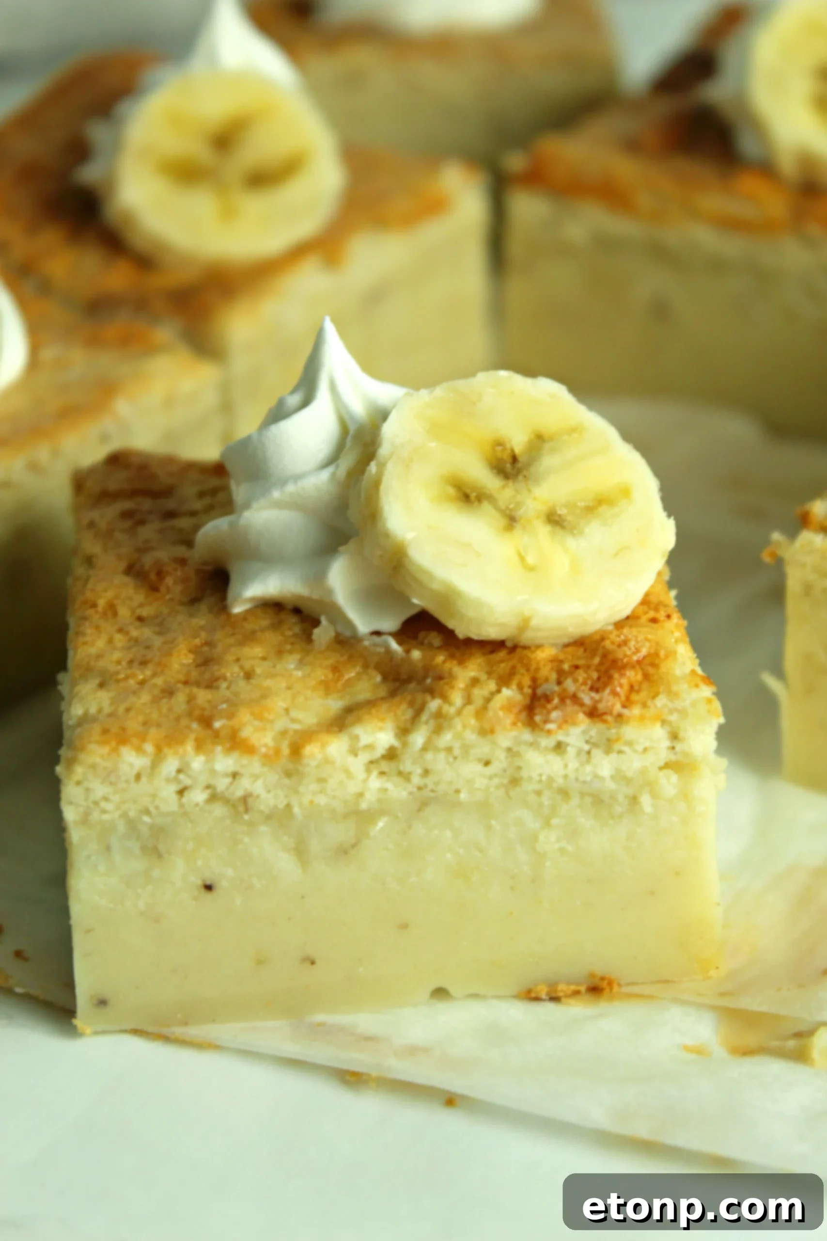 A beautifully sliced Banana Magic Cake revealing its three distinct layers, served on a white plate with fresh banana slices and whipped cream.