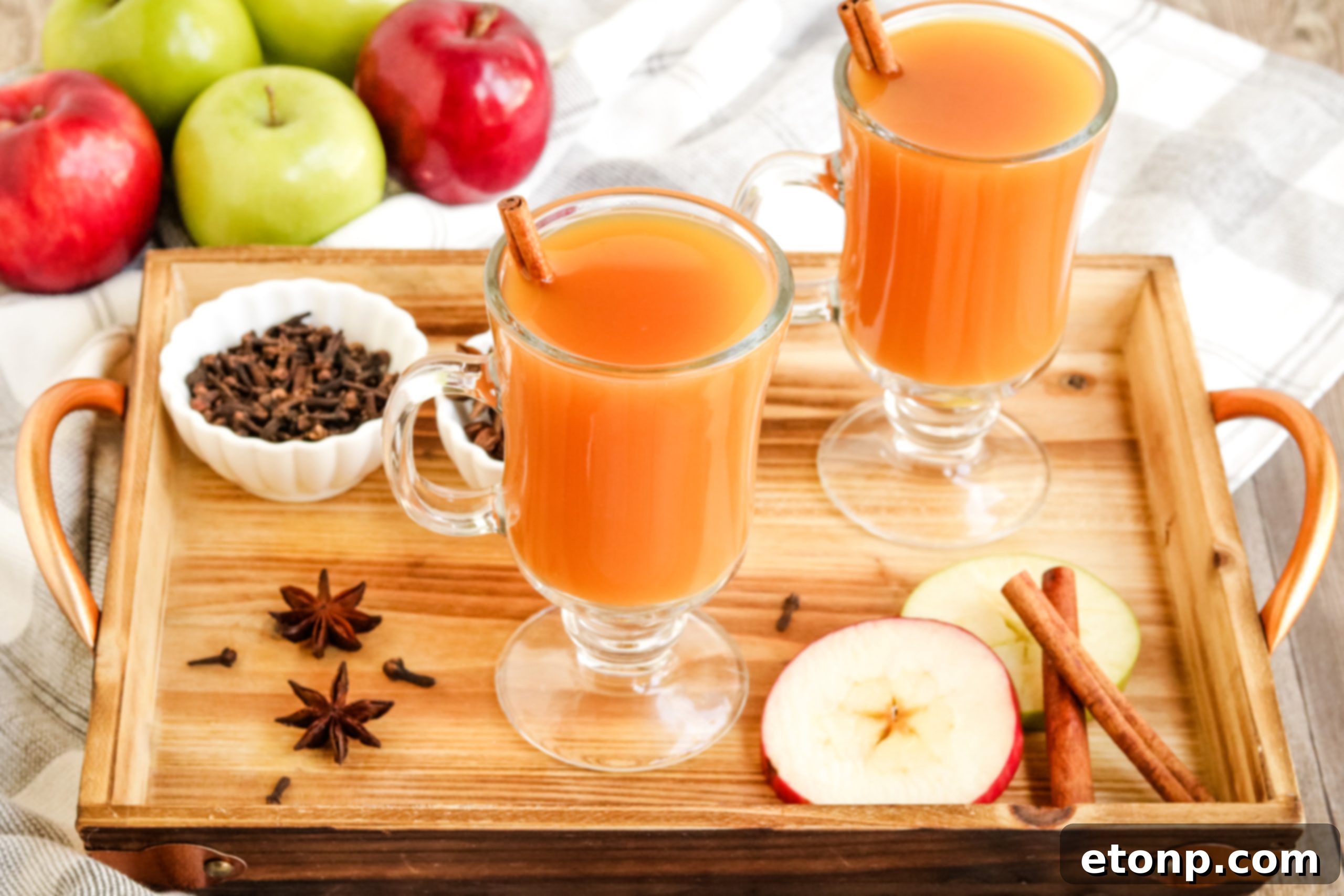 A festive table setting with hot mulled cider in clear mugs, decorated with cinnamon sticks and star anise, surrounded by seasonal decor.