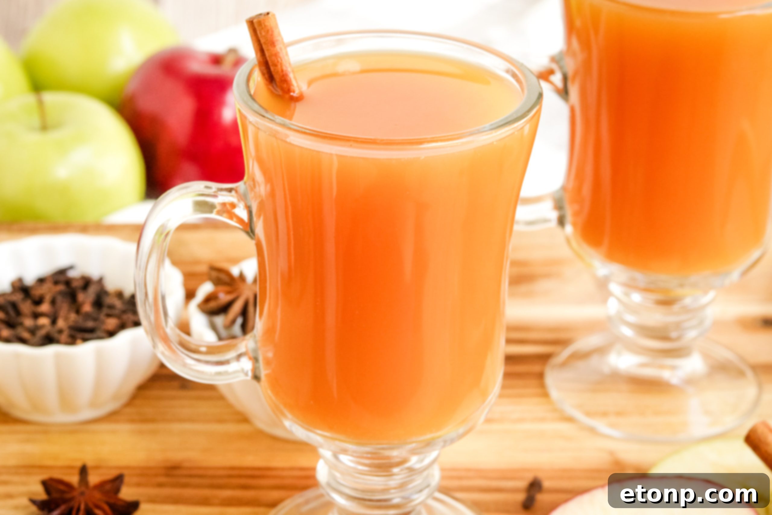 Two mugs of mulled cider, one plain and one with a shot of rum or brandy being added, on a cozy background.