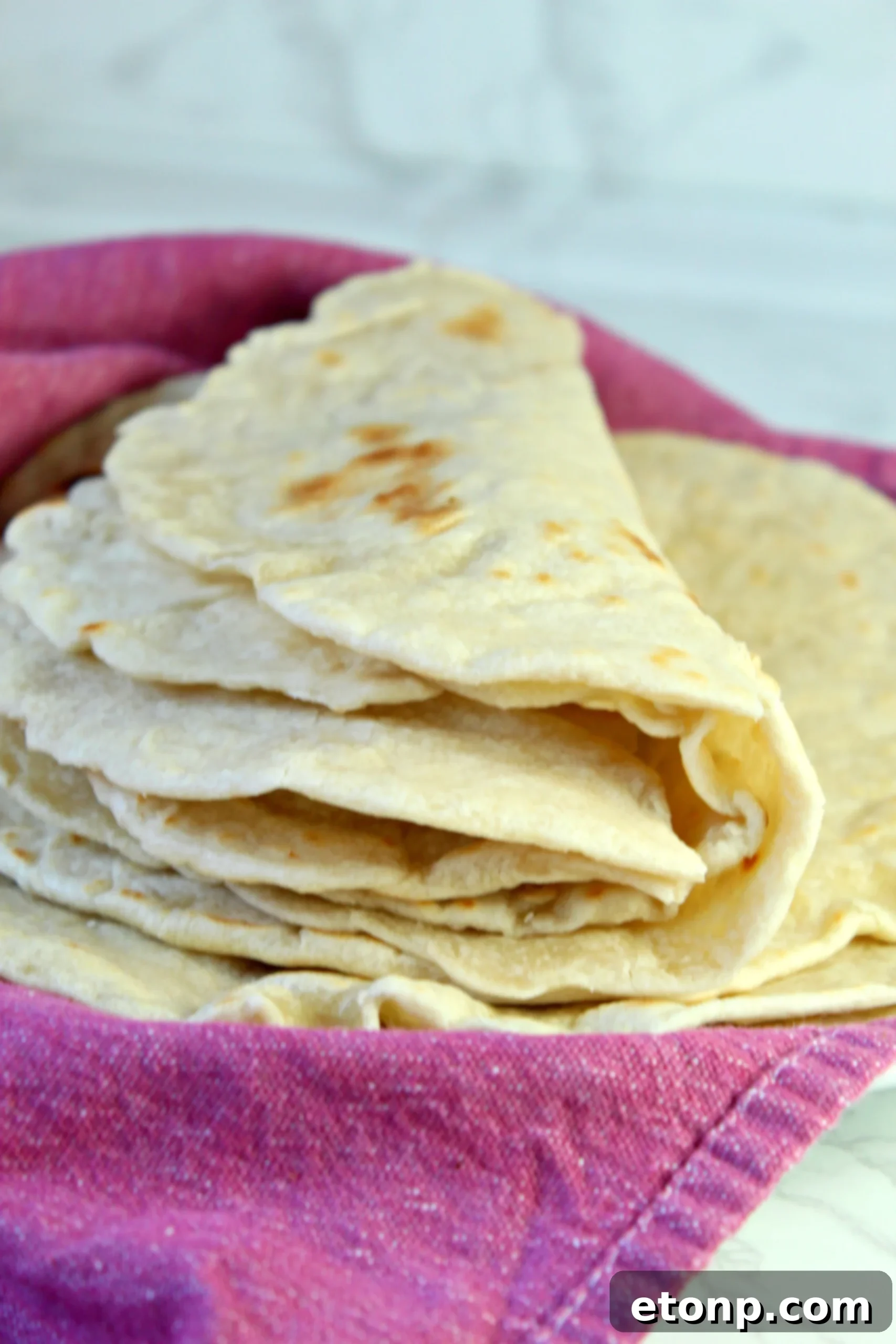 Freshly made homemade flour tortillas stacked on a plate, highlighting their soft texture.