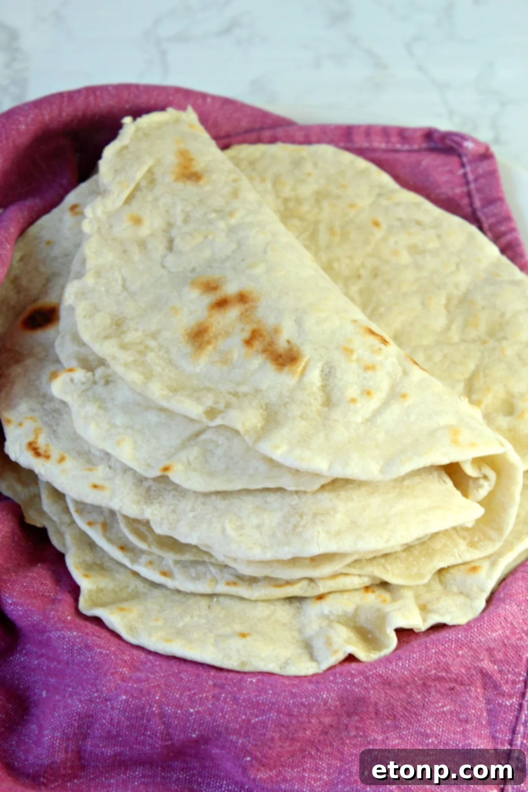 Close-up of a stack of freshly cooked homemade flour tortillas, showcasing their smooth edges and soft appearance.