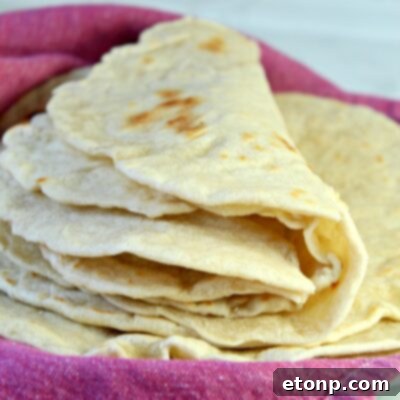 A stack of perfectly golden brown homemade flour tortillas, highlighting their fresh appearance.