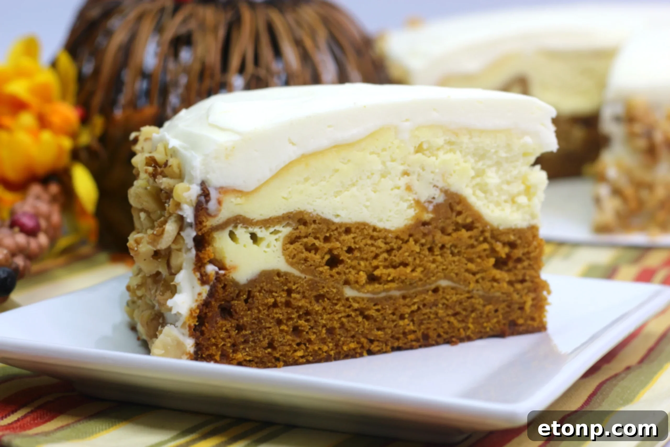 A close-up of the side of the Pumpkin Cake Cheesecake, revealing the distinct layers of pumpkin cake and creamy cheesecake filling, garnished with chopped walnuts