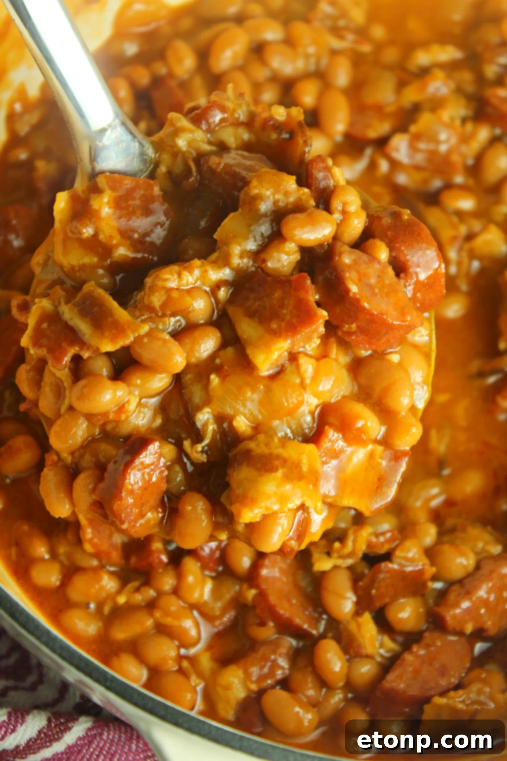 A close-up shot of delicious baked beans with smoked sausage, garnished with fresh herbs, in an oven-safe dutch oven.