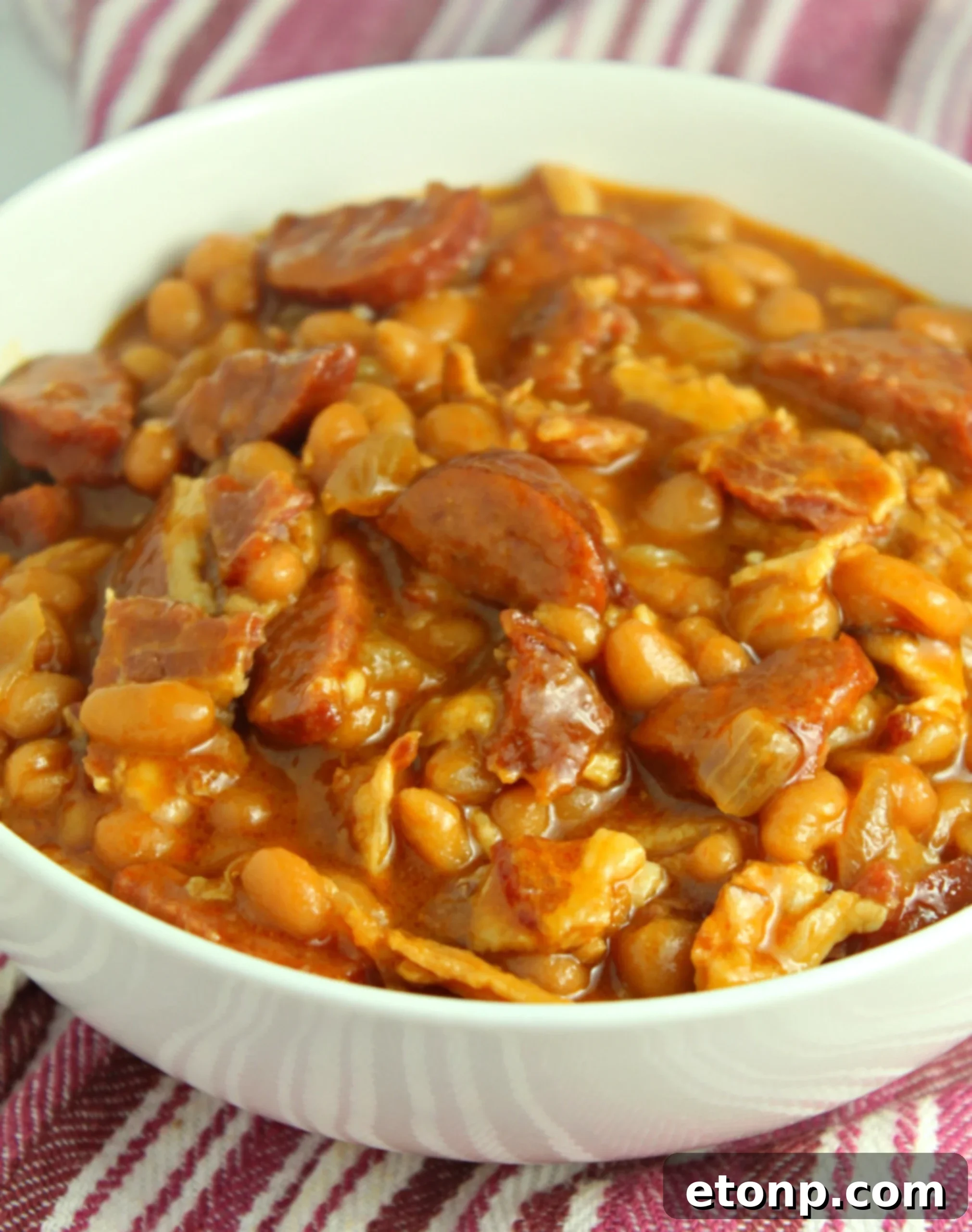 A close-up of the rich, thick texture of baked beans with sausage, showing the individual bean and meat pieces.