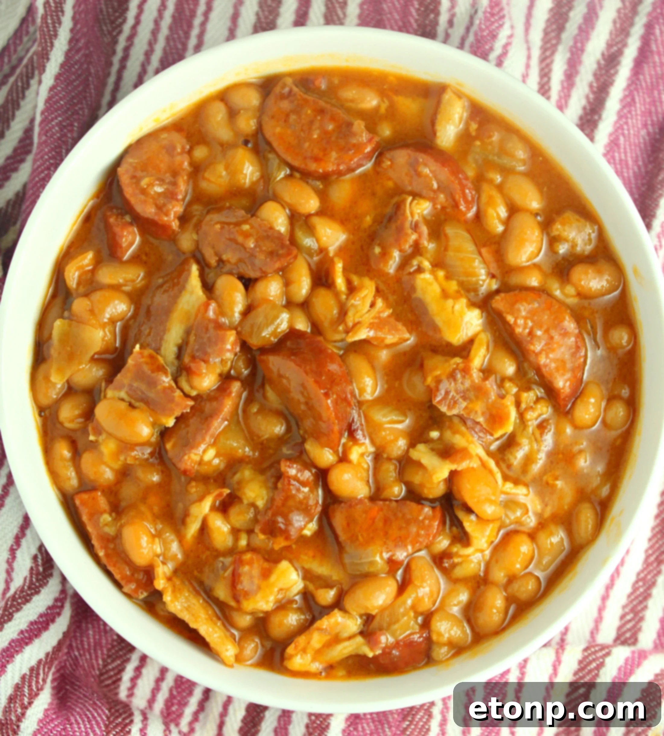 A large serving spoon scooping out a portion of the baked beans with smoked sausage from the dutch oven.