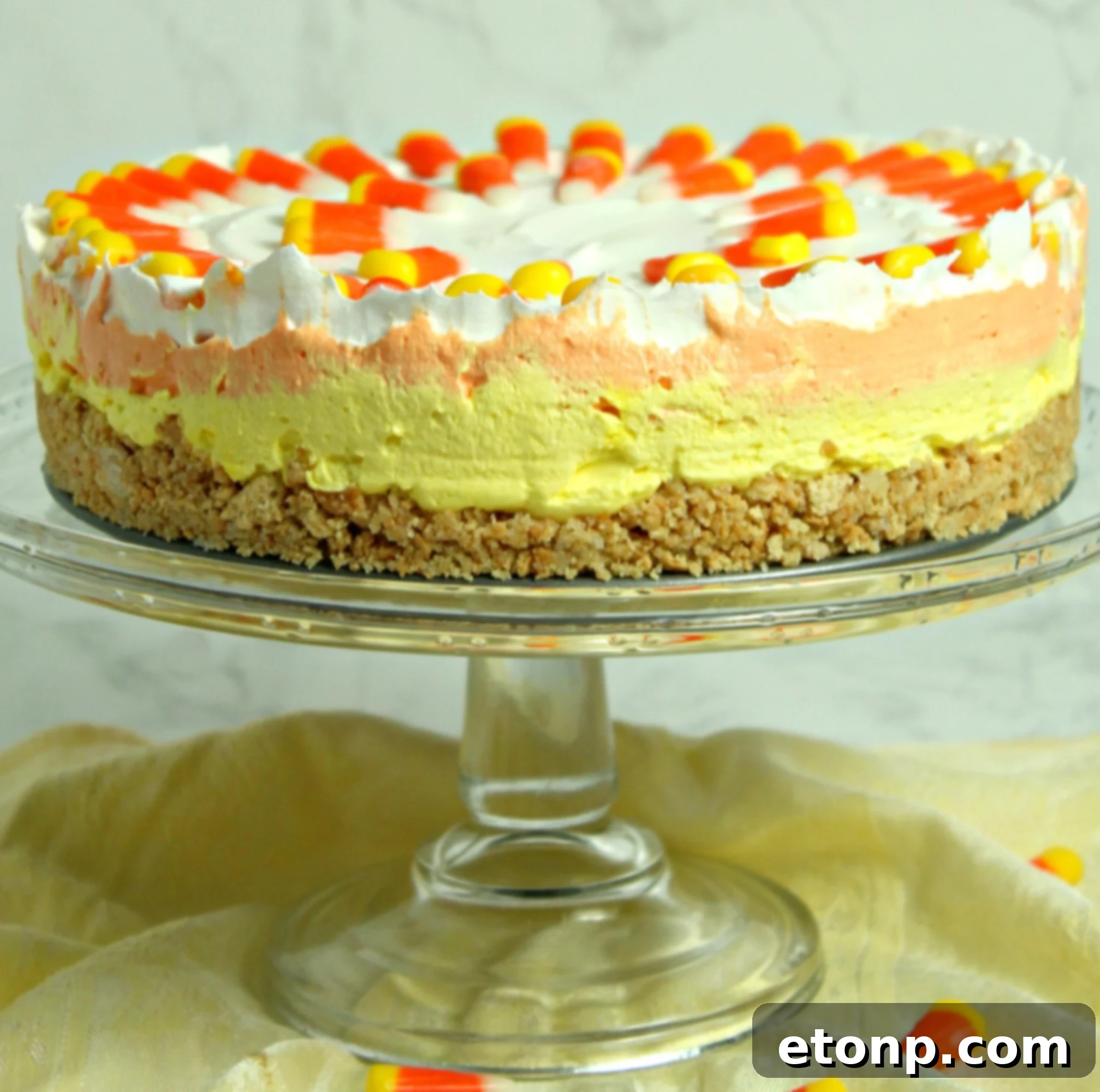 Close-up of a slice of No-Bake Candy Corn Cheesecake on a white plate, showing the creamy layers