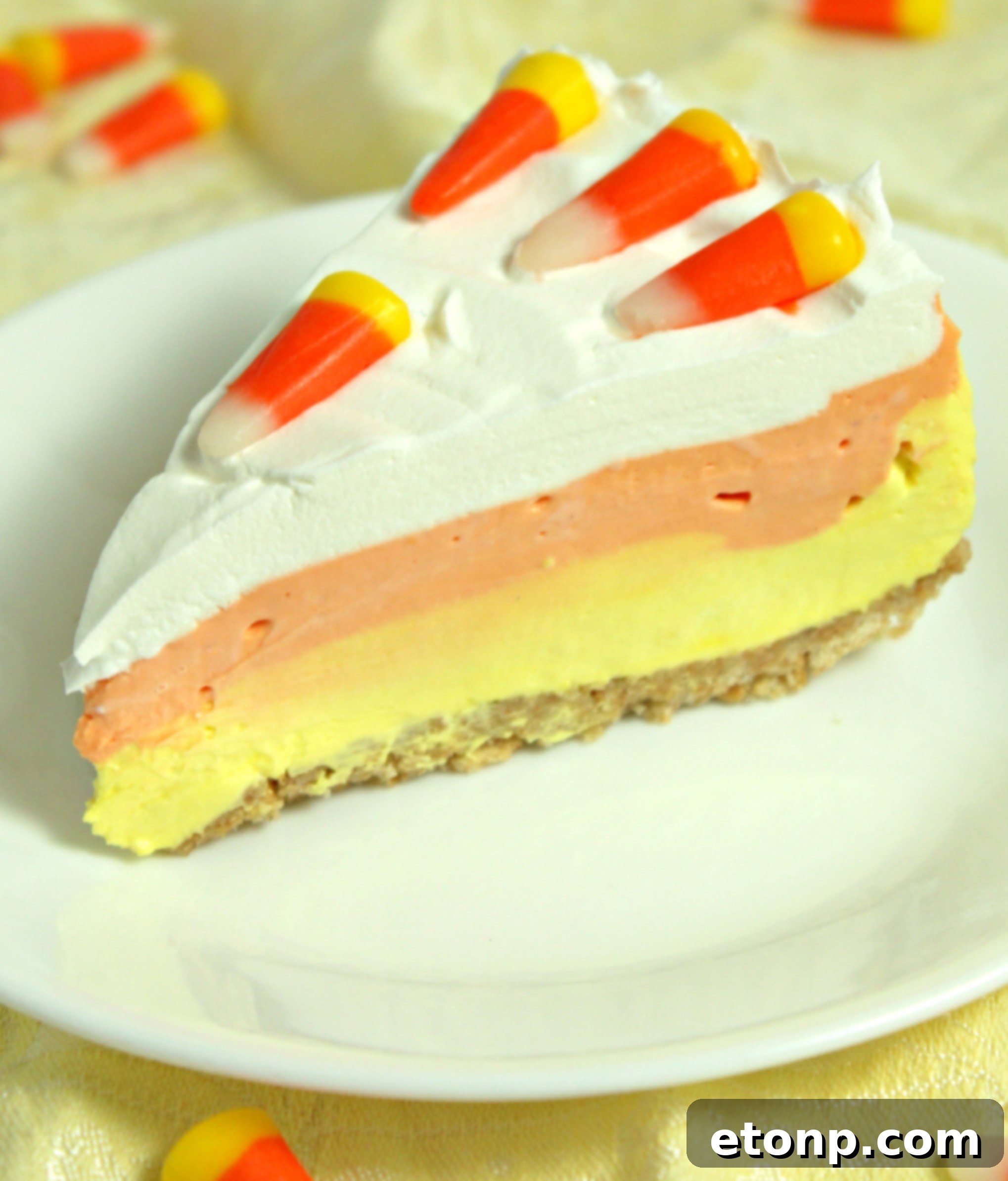 A close-up of a generous slice of the layered Candy Corn Cheesecake, showing its fluffy texture and vibrant colors.