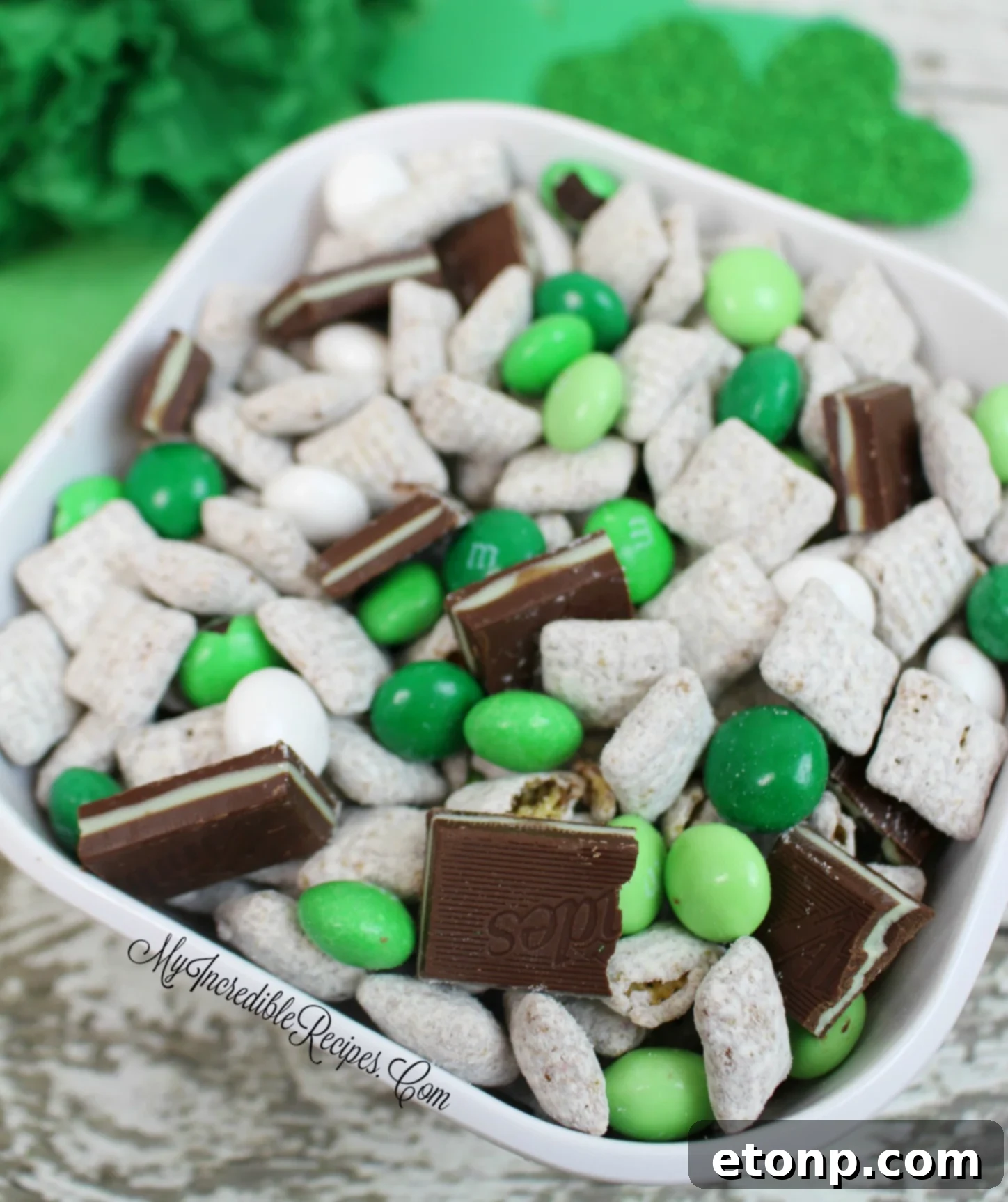 A bowl overflowing with Andes Mint Muddy Buddies, highlighting the vibrant green mint M&M's and crushed Andes Mint pieces mixed in.