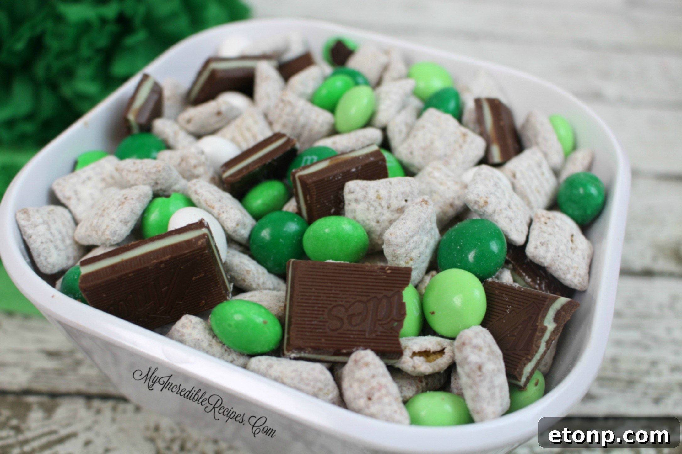 Close-up of a serving of Andes Mint Muddy Buddies, showcasing the texture of the cereal, the powdered sugar, and the colorful mint candies.