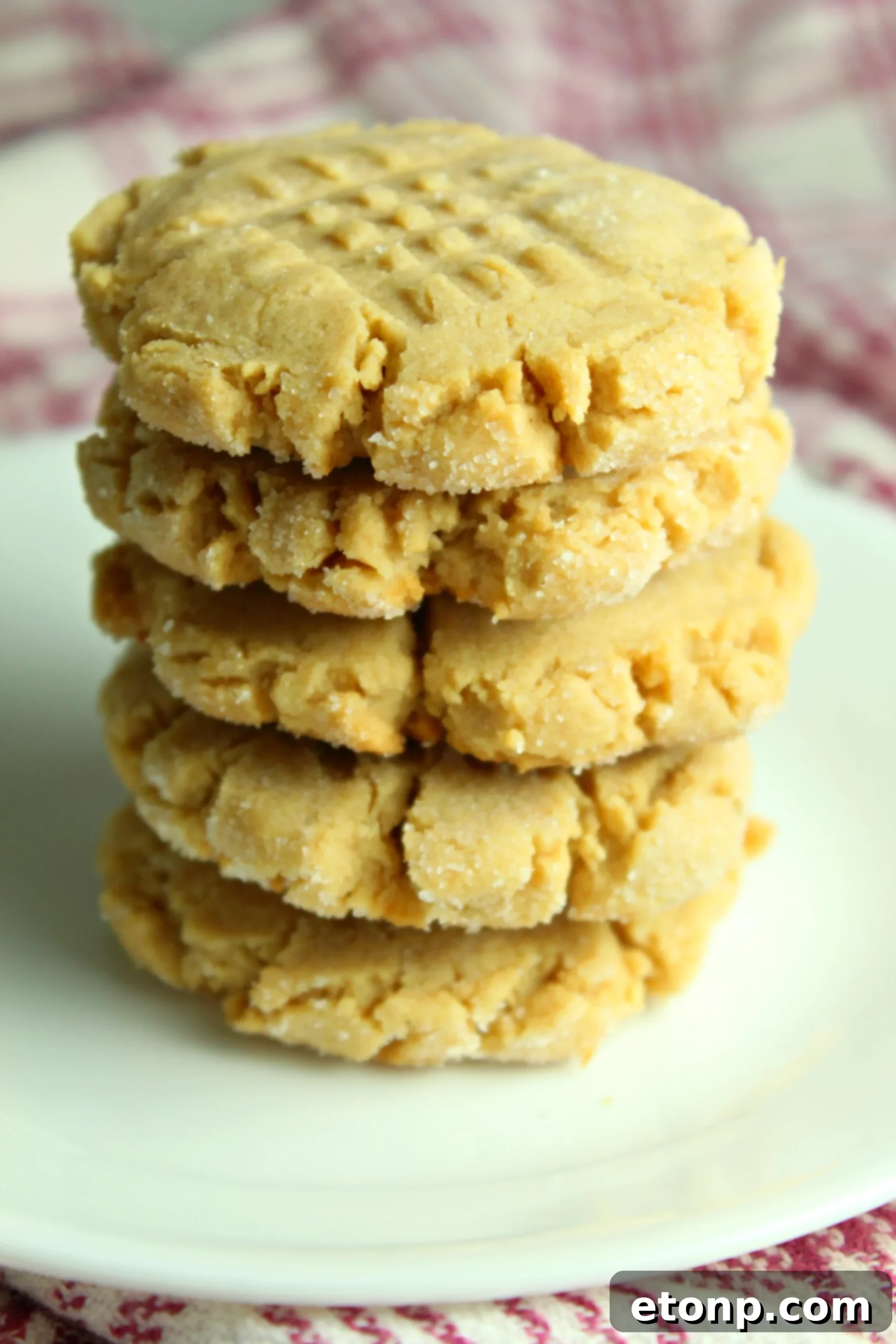 A stack of perfectly baked, soft and chewy classic peanut butter cookies, showing the signature criss-cross pattern.