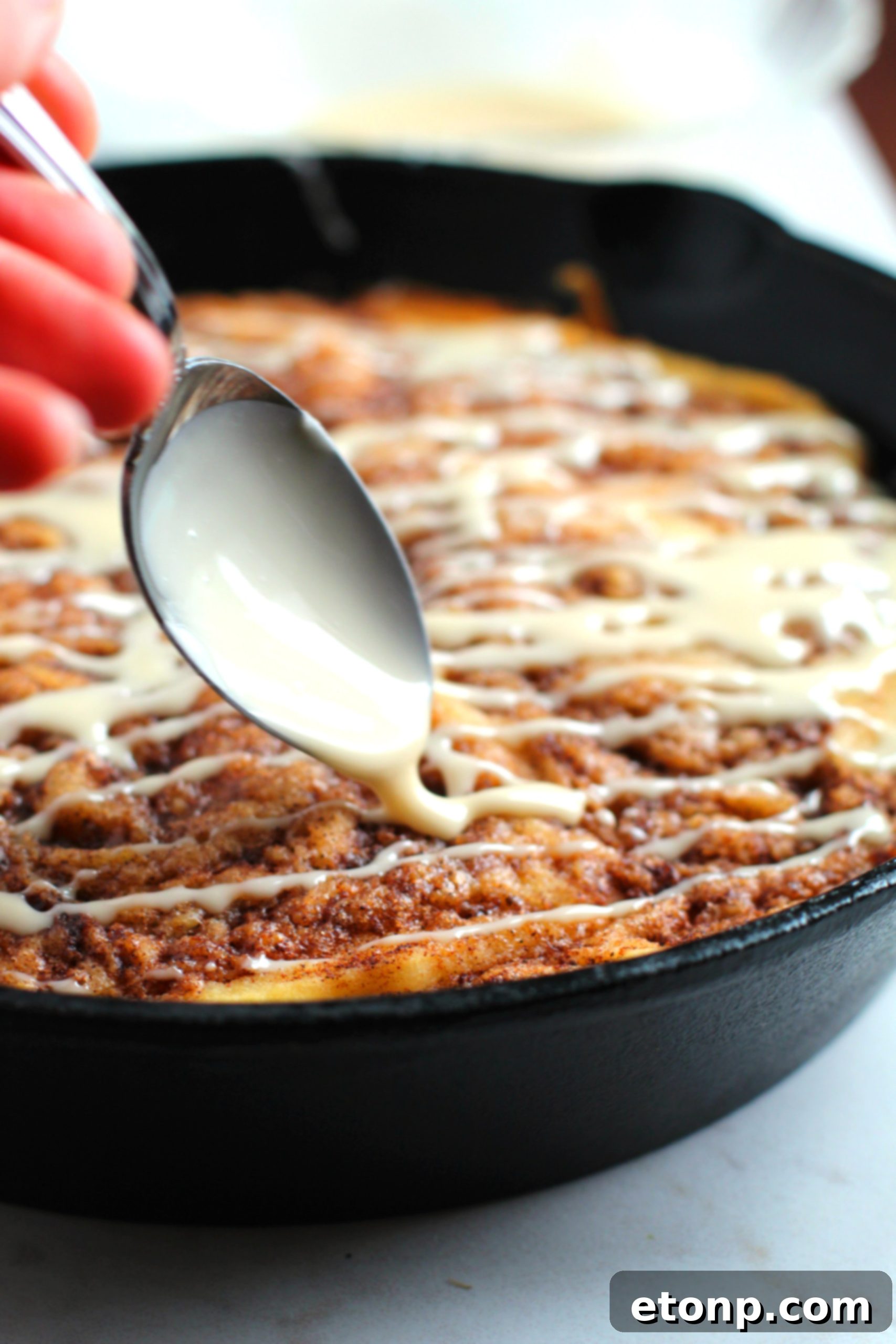 Warm Cinnamon Swirl Skillet Delight 5 Overhead view of the full skillet cake, glistening with vanilla icing.