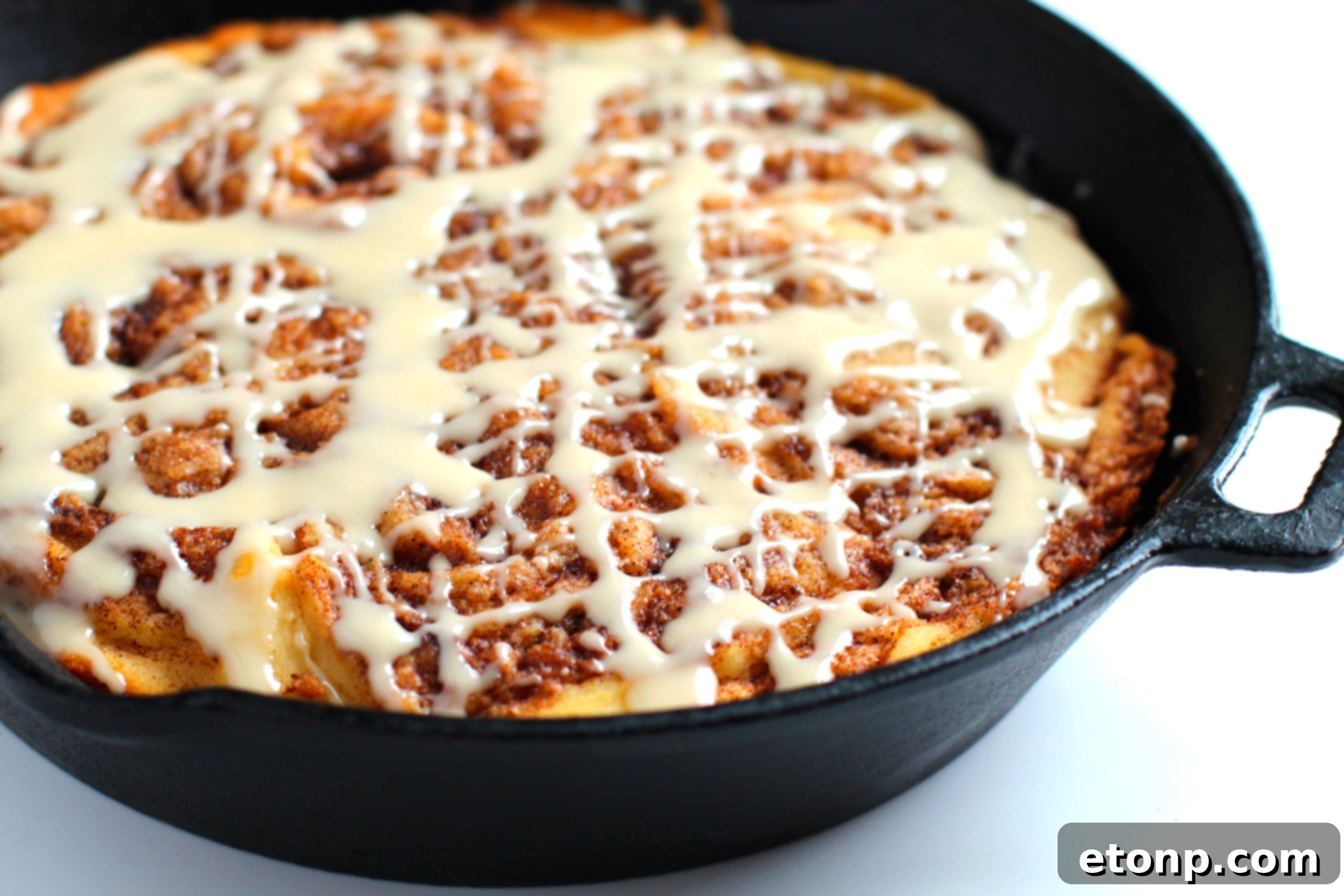 Warm Cinnamon Swirl Skillet Delight 6 Cinnamon Roll Skillet Cake with a generous drizzle of vanilla icing, ready to be enjoyed.