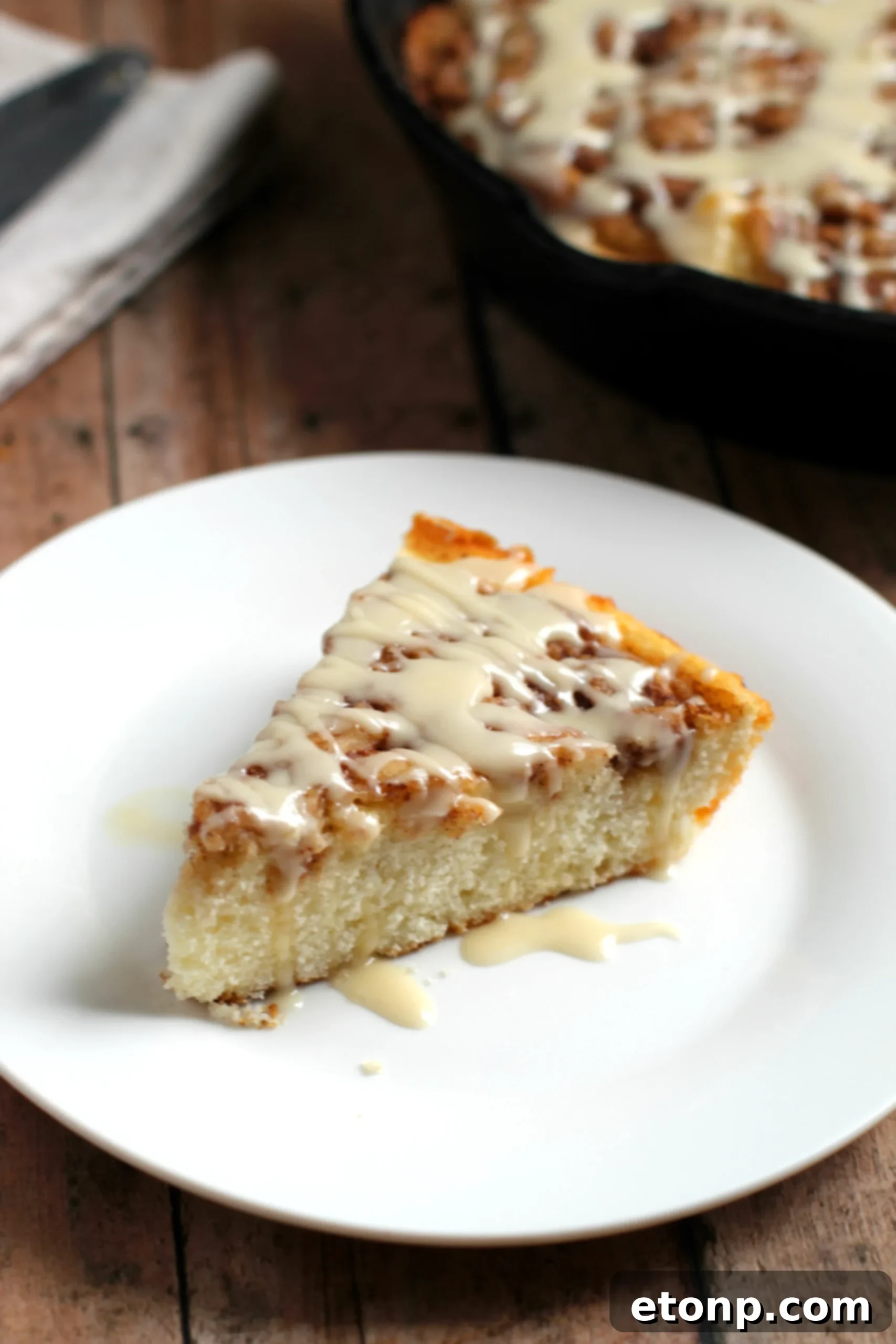 Warm Cinnamon Swirl Skillet Delight 7 A close-up of a warm slice of Cinnamon Roll Skillet Cake with abundant gooey cinnamon and icing.