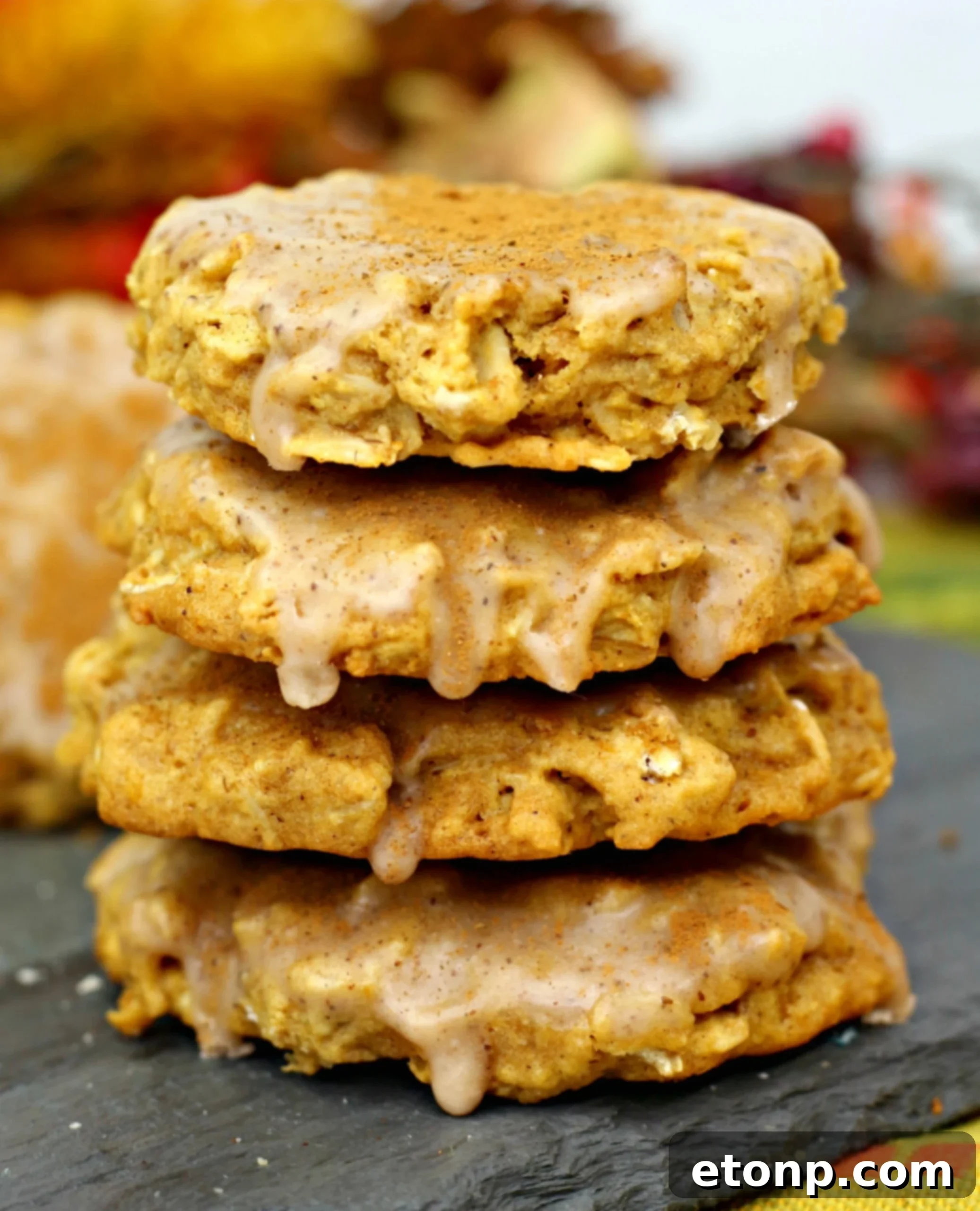 Close-up of a stack of Iced Pumpkin Oatmeal Cookies with a bite taken out of the top one, showing the chewy interior and creamy icing.