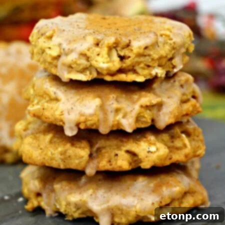 A close-up of a stack of Iced Pumpkin Oatmeal Cookies with a bite taken out of the top one, showing the chewy interior and creamy icing.